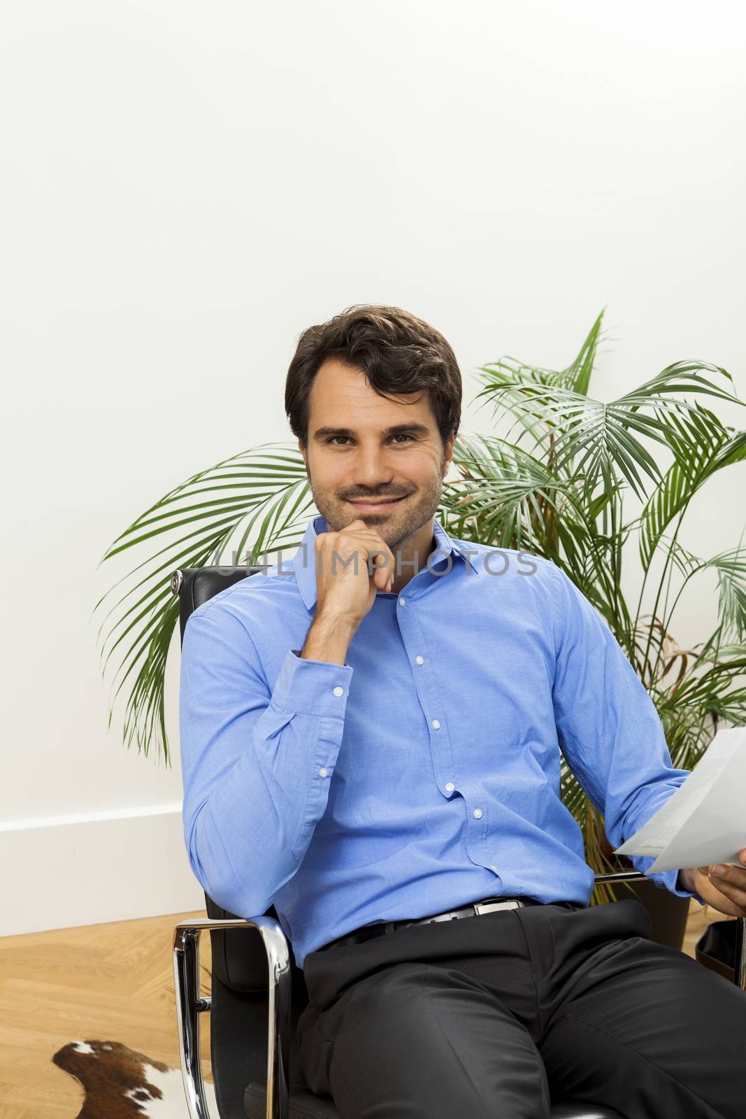 Young handsome man sitting at his desk in the office while reading written agreements and studying important documentation for work