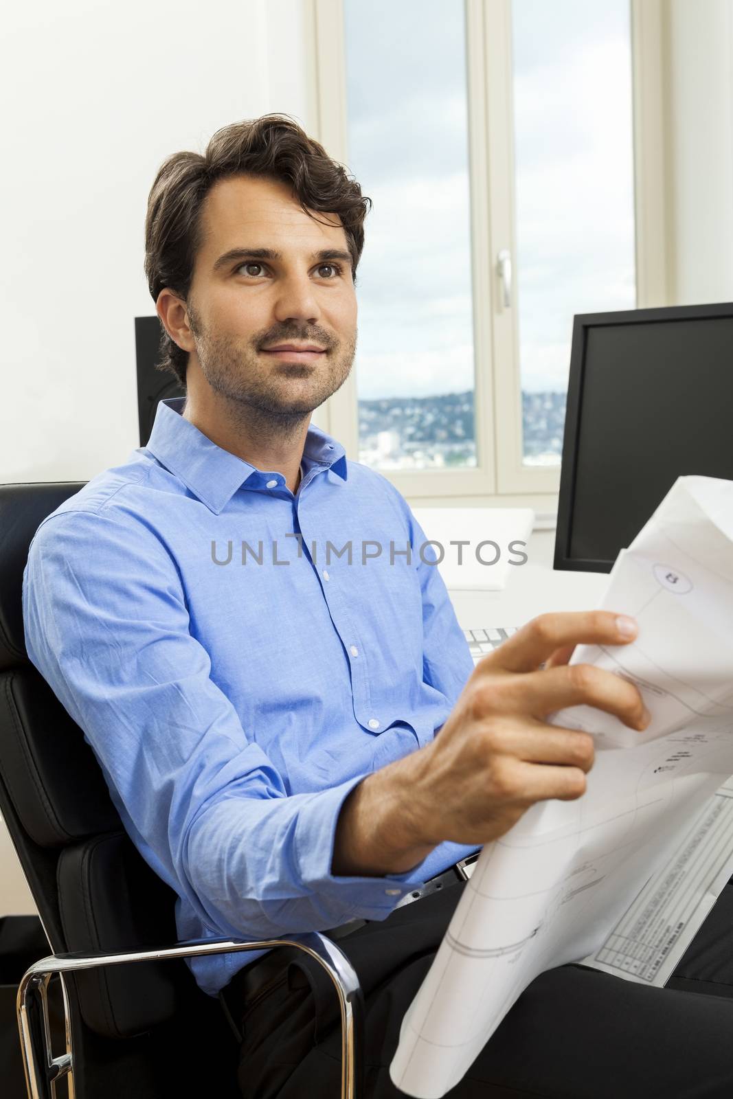 Young handsome man sitting at his desk in the office while reading written agreements and studying important documentation for work