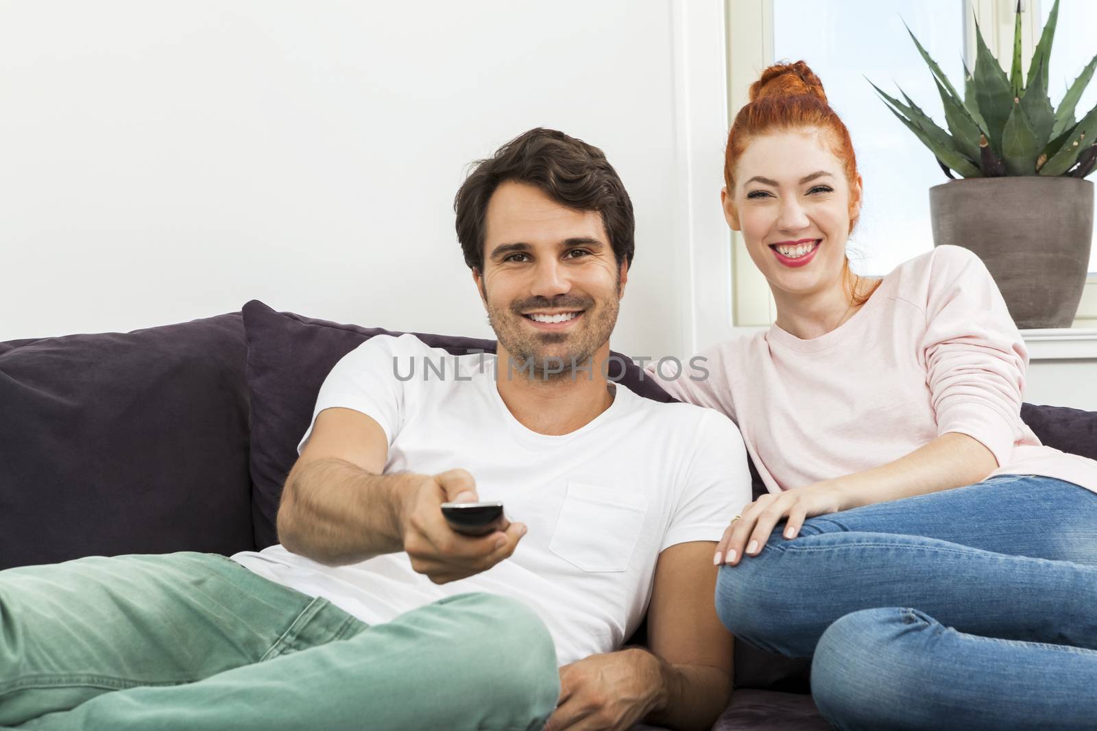 Happy Young Sweet Couple in Casual Clothing Smiling at Each Other While Sitting at the Couch in the Living Room