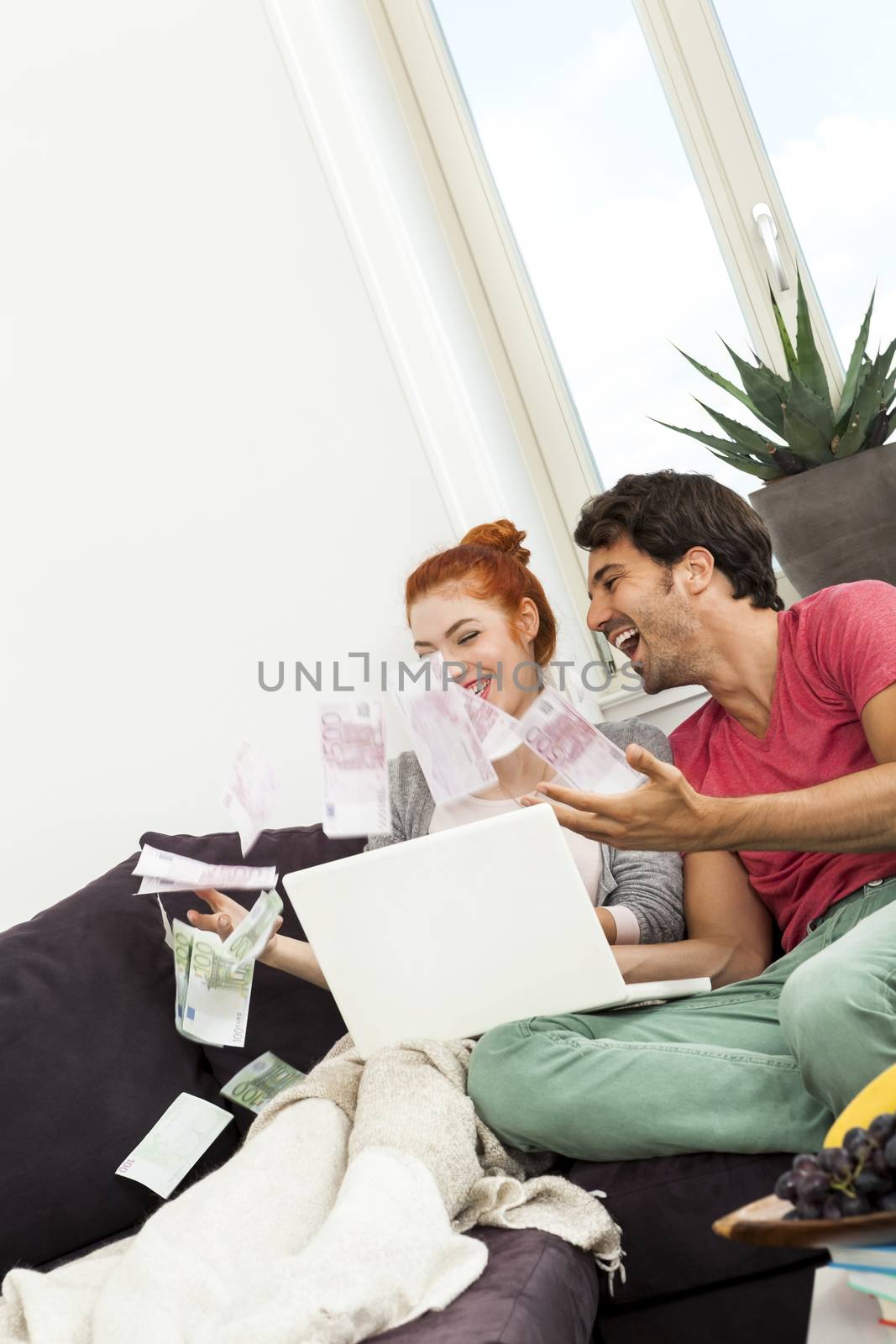 Close up Very Happy Young Couple with Laptop Sitting at the Couch and Throwing Euro Money in the Air.