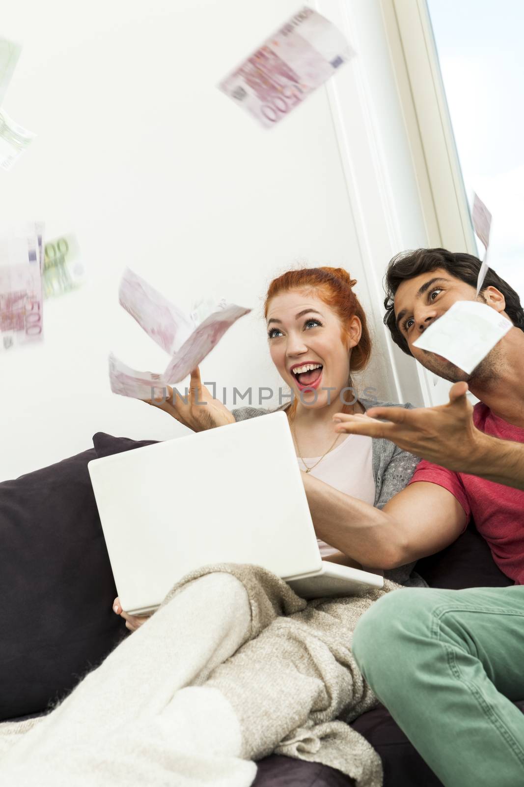 Close up Very Happy Young Couple with Laptop Sitting at the Couch and Throwing Euro Money in the Air.