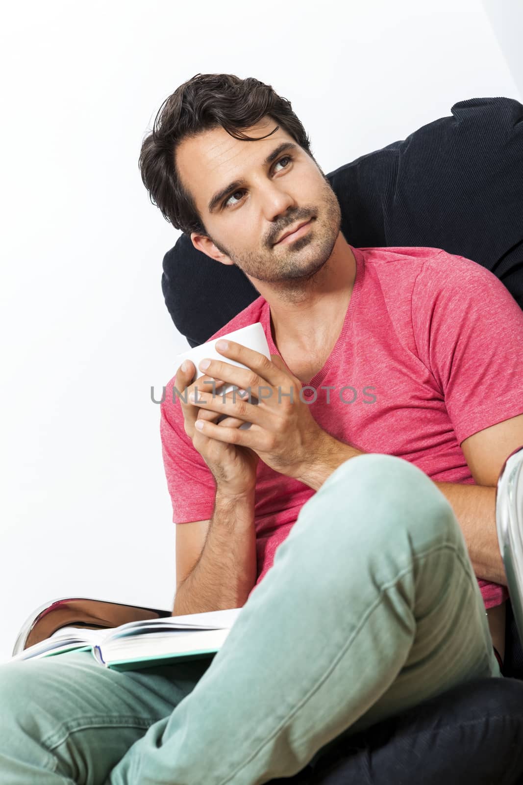 Young Man in Casual Clothing Sitting on Black Chair While Reading a Book and Holding a Glass of Drink.