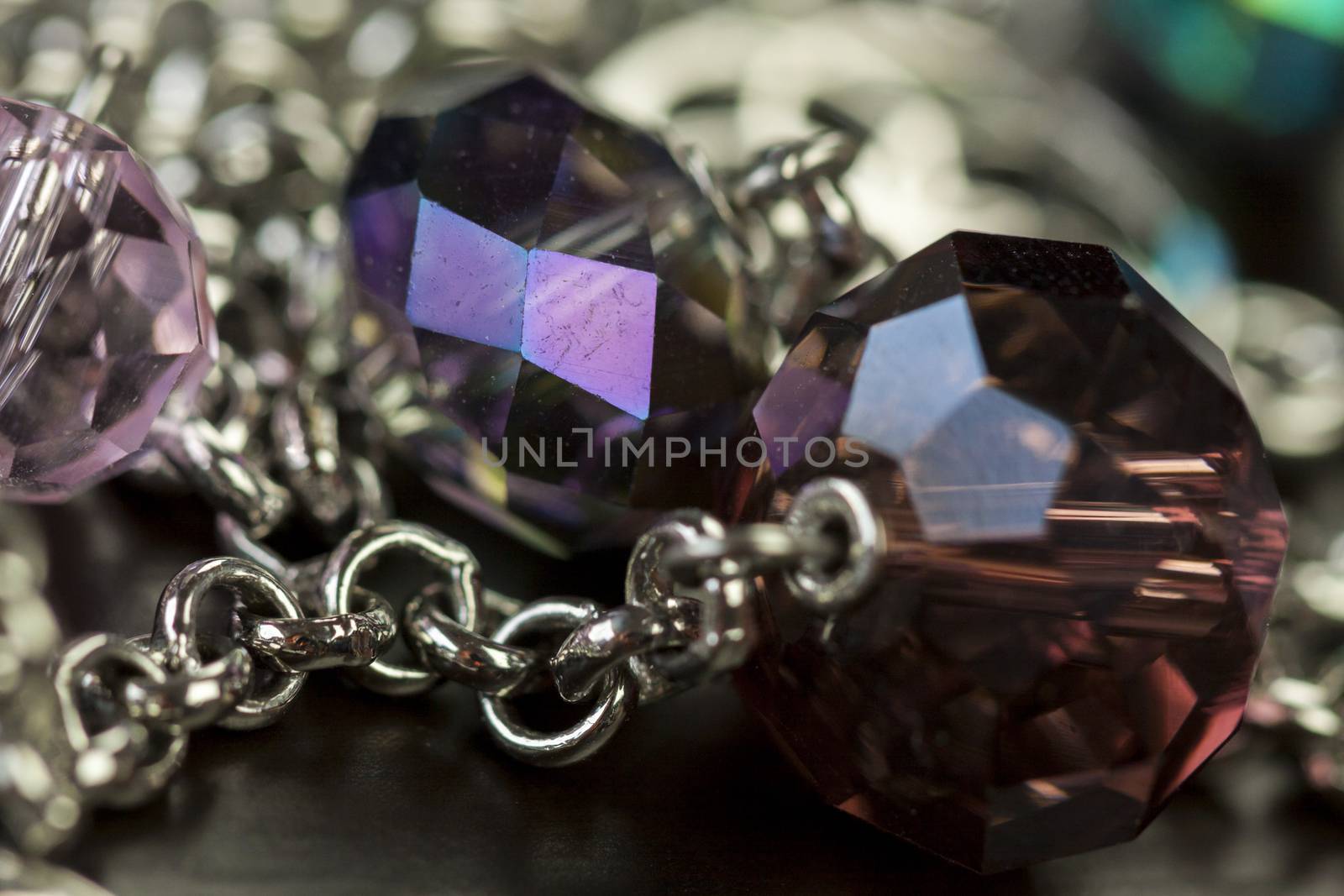 Close up of three attractive shiny purple beads attached by silver chains on an item of jewellery in a fashion and handicraft concept