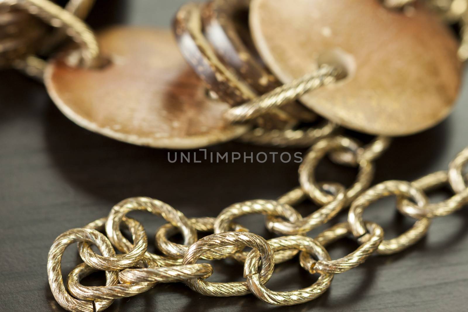 Scratched and tarnished old silver jewellery with two flat discs flanking a ring suspended on an oval link chain, close up view on a grey background