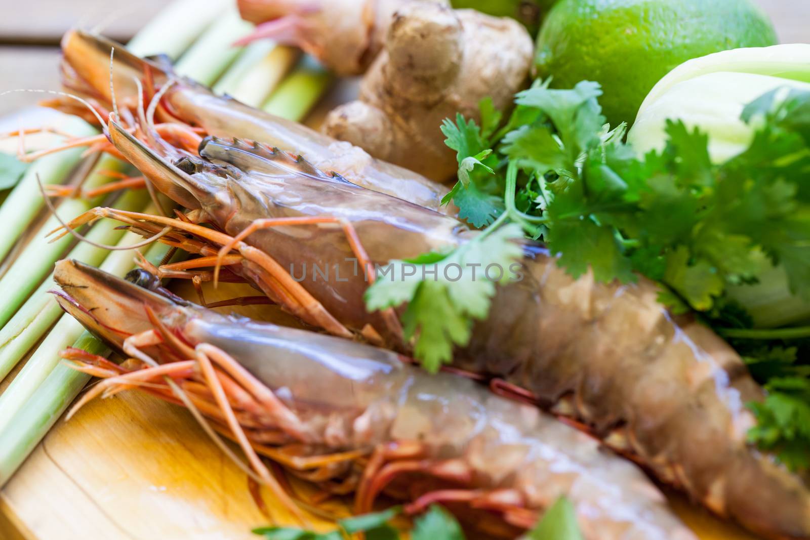 Ingredients for Thai tom yam soup laid out on a kitchen counter with tiger prawns, mushrooms, ginger, lemongrass, limes, celery, parsley and spices