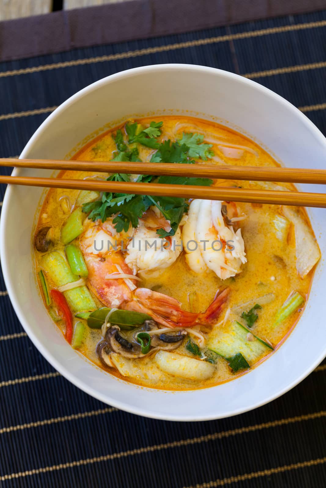 Bowl of traditional Thai tom yam soup with vegetables and prawns in a spicy aromatic broth served with chopsticks