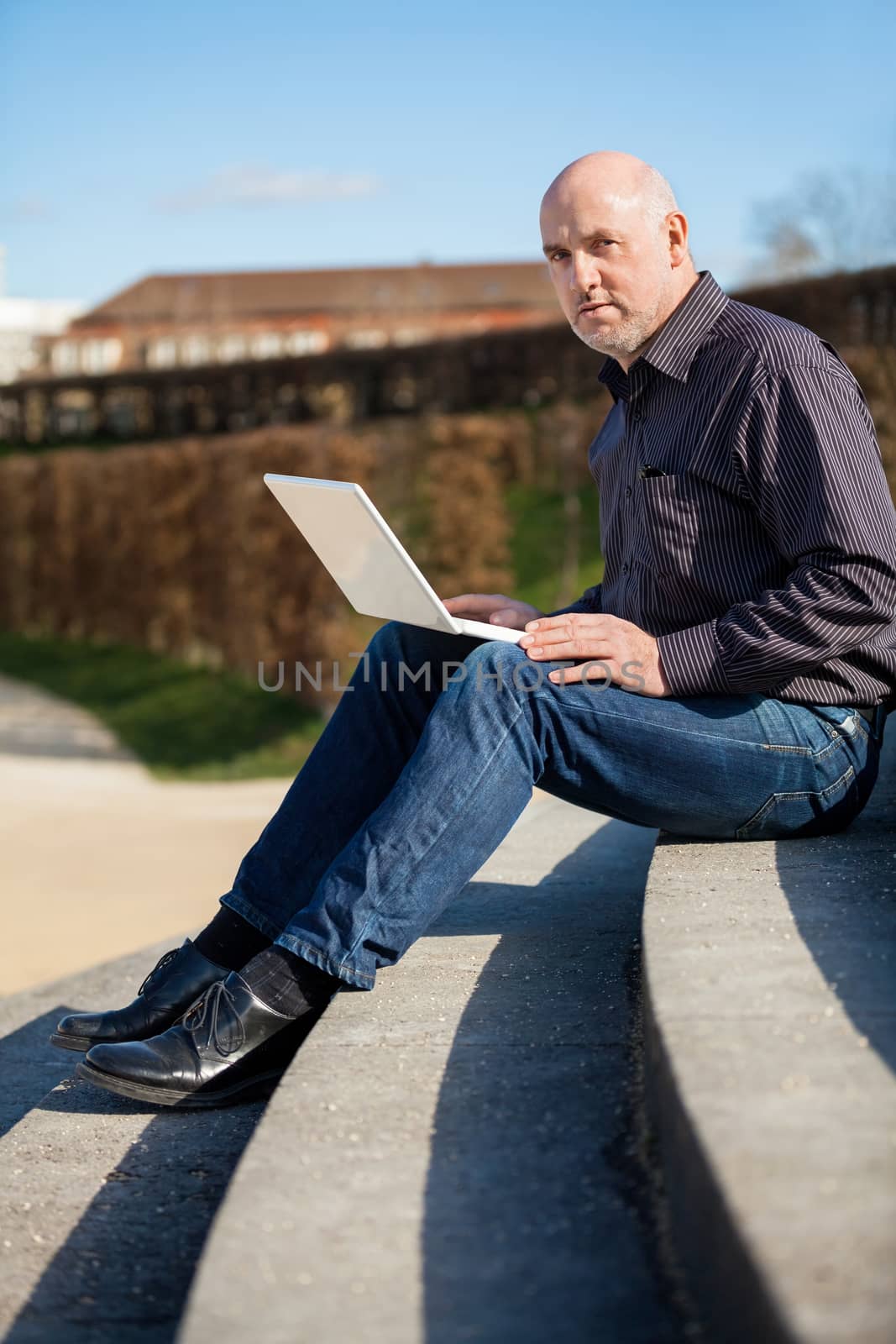 High angle profile view of a balding middle-aged man sitting on a wooden bench using a laptop computer