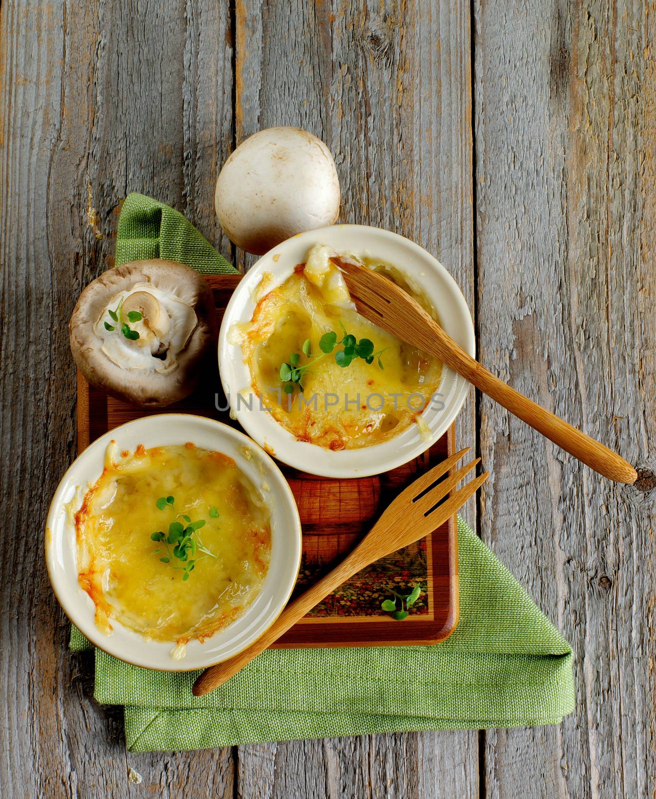 Arrangement of Mushroom Julienne in Ramekins with Raw Champignons and Wooden Forks and Napkin on Rustic Wooden background. Top View