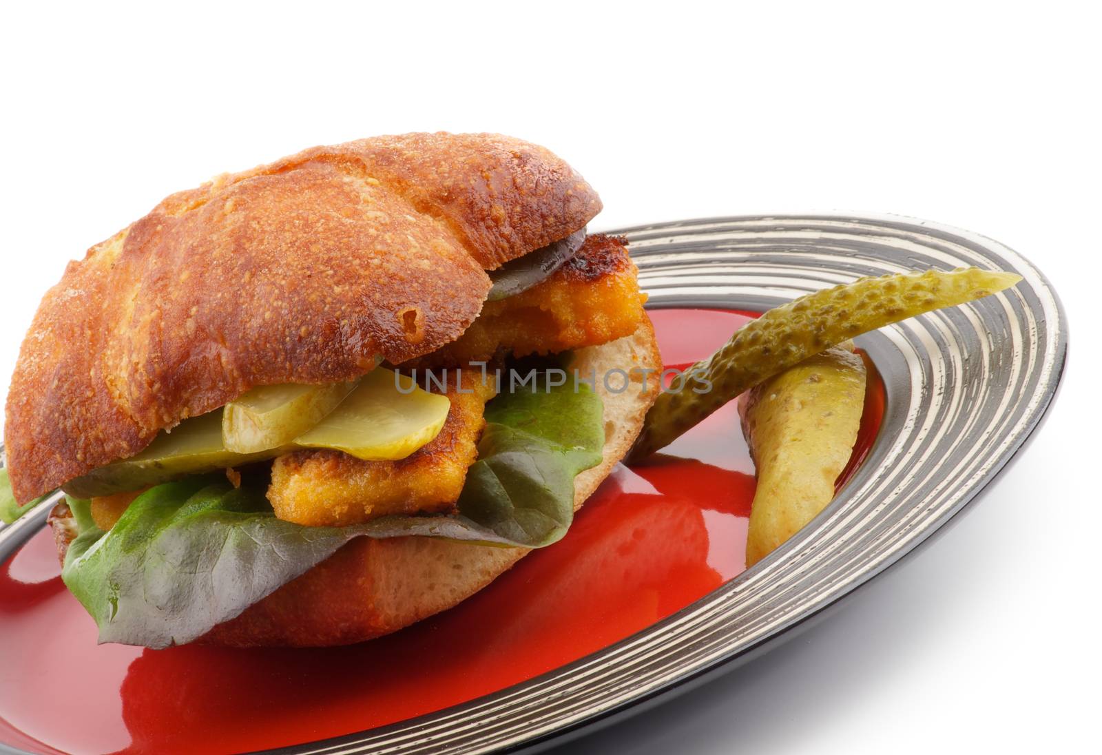 Homemade Fish Burger with Fish Sticks, Lettuce, Gherkins and Whole Wheat Bread on Red Stripped Plate closeup on white background