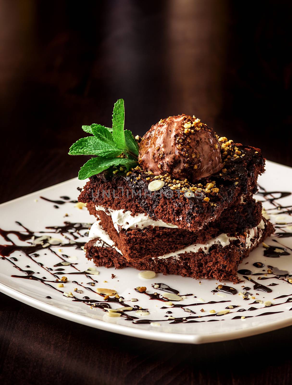 Chocolate brownie cake with a scoop of ice cream with a mint leaf on a white plate