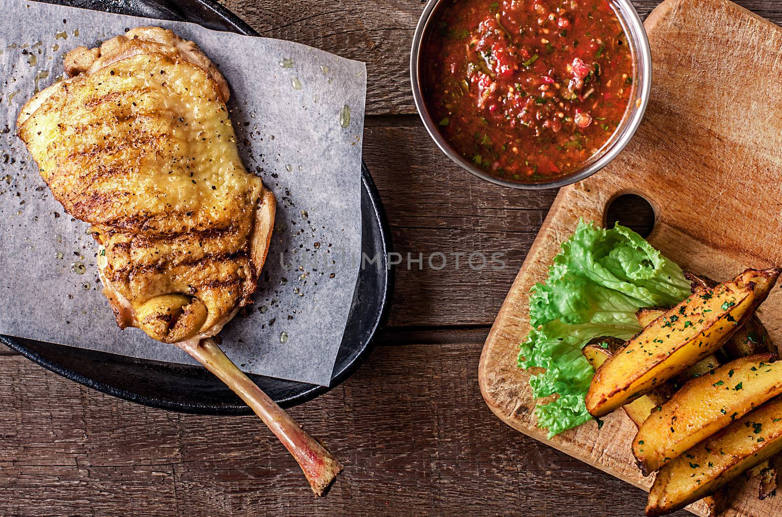 Fried chicken meat on the bone, red sauce, potato wedges, lettuce on background wooden table