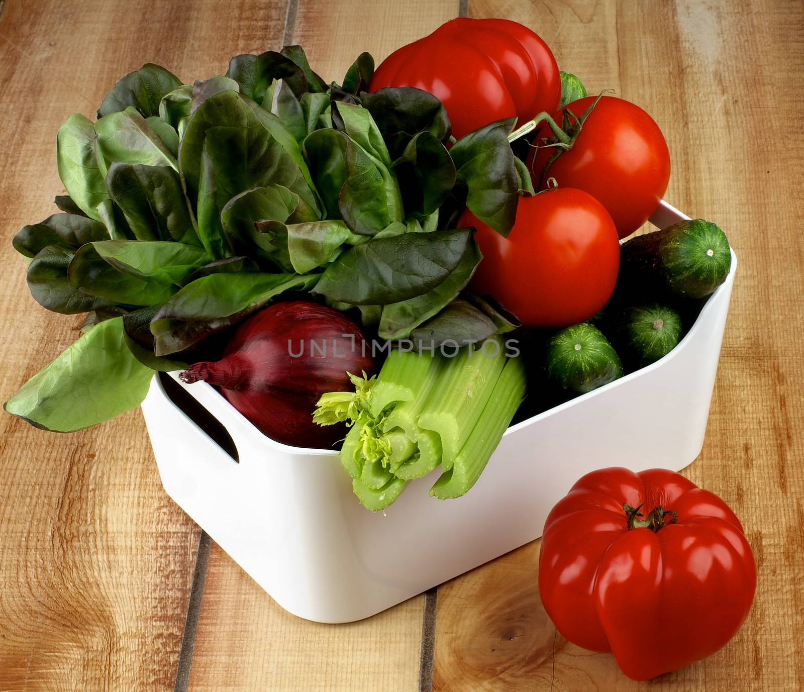 Arrangement of Celery, Cucumbers, Tomatoes, Red Onion and Butterhead Lettuce in White Plastic Container on Rustic background