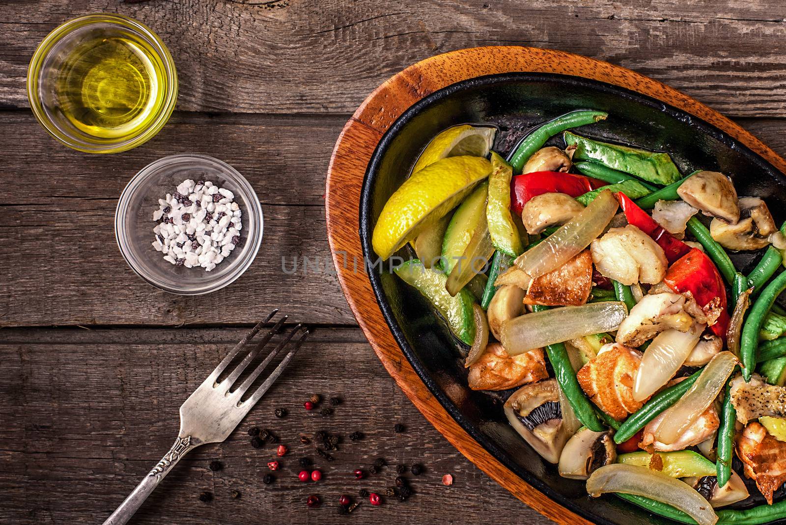 Stew chicken with vegetables and mushrooms on a wooden table with fork, pepper, salt, olive oil