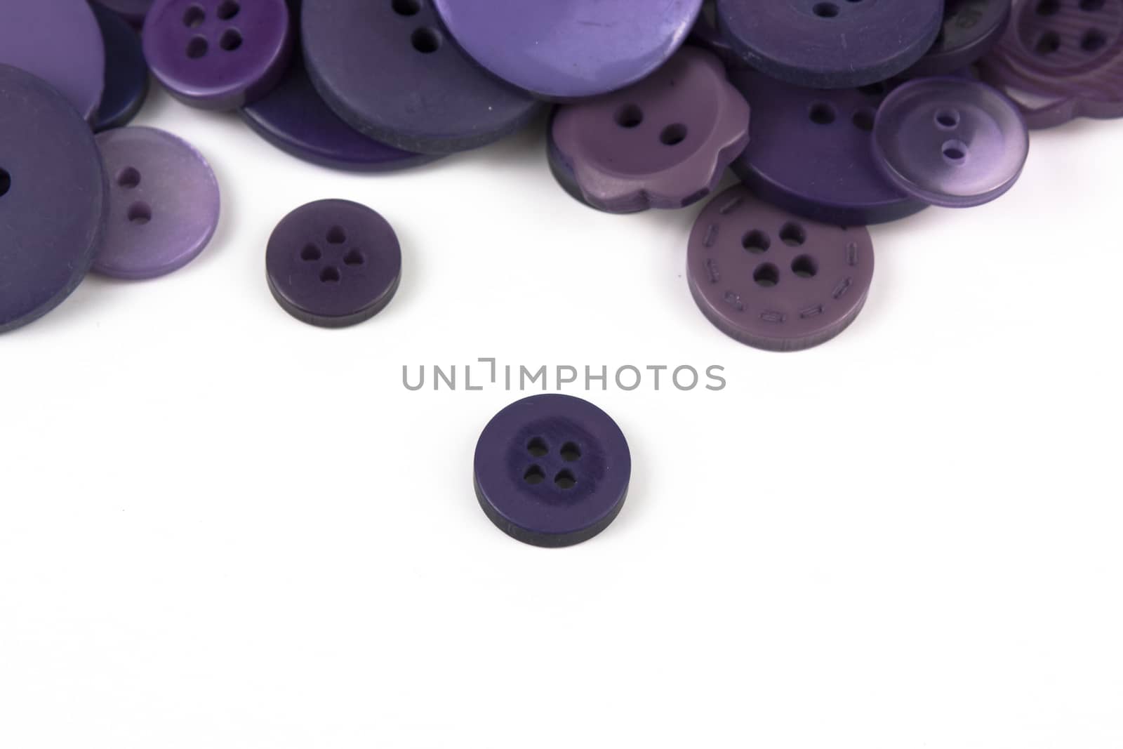 Close up of various purple button scattered on a white surface.