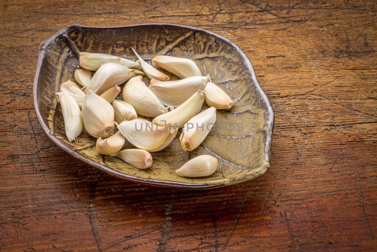 garlic cloves on a ceramic leaf shaped bowl against rustic wood