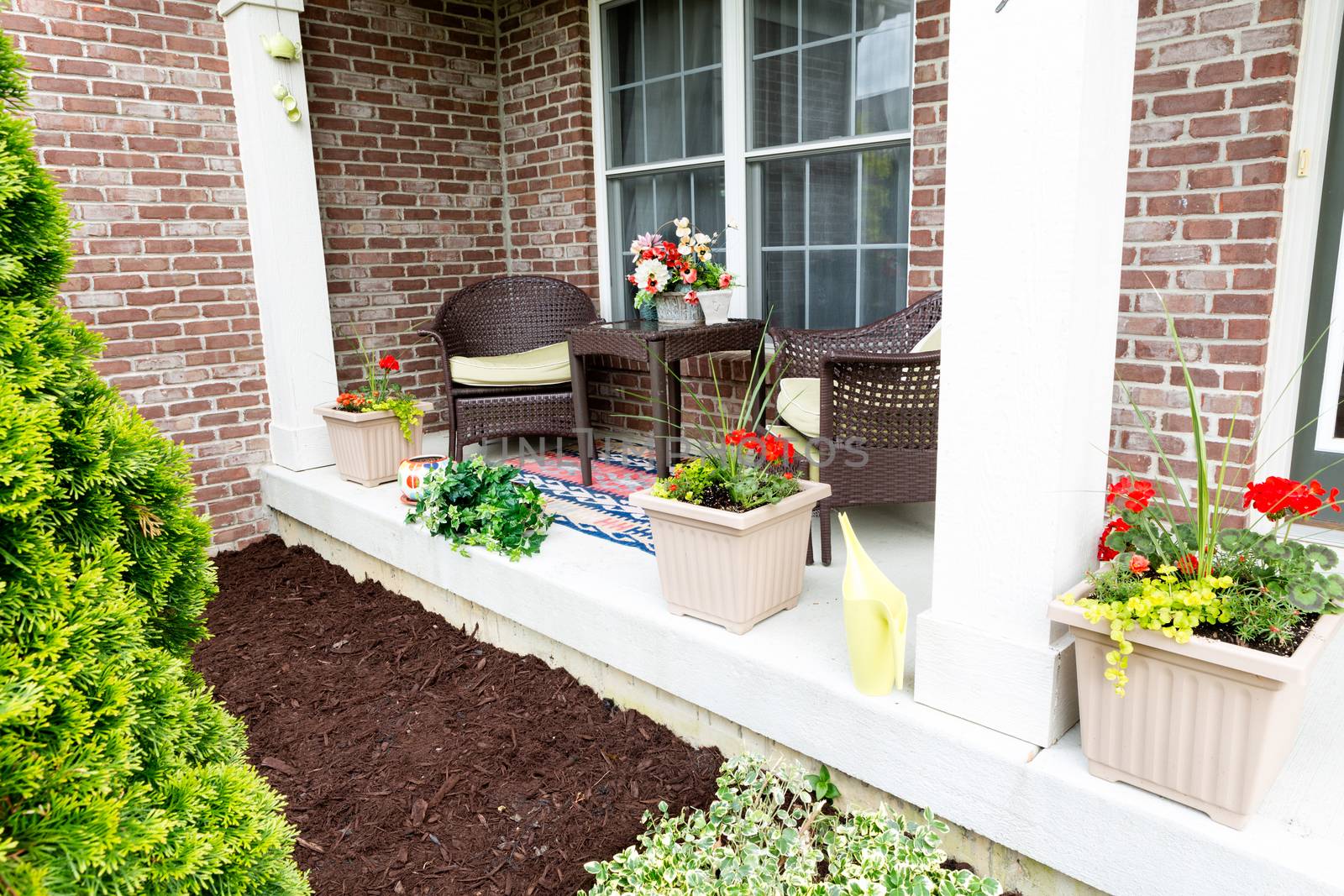 Mulching flowerbeds around the house with a freshly mulched bed alongside an open-air patio decorated with ornamental flowers