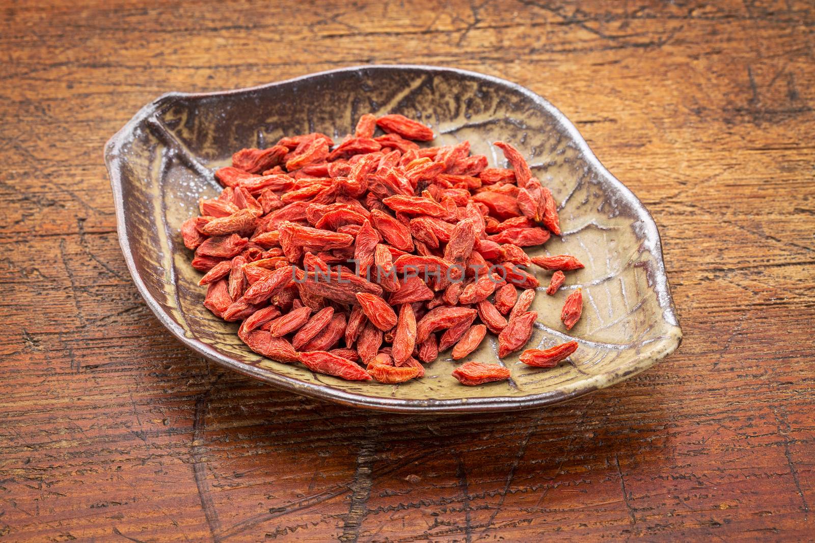 dried goji berries (wolfberry in a leaf shaped ceramic bowl against rustic wood