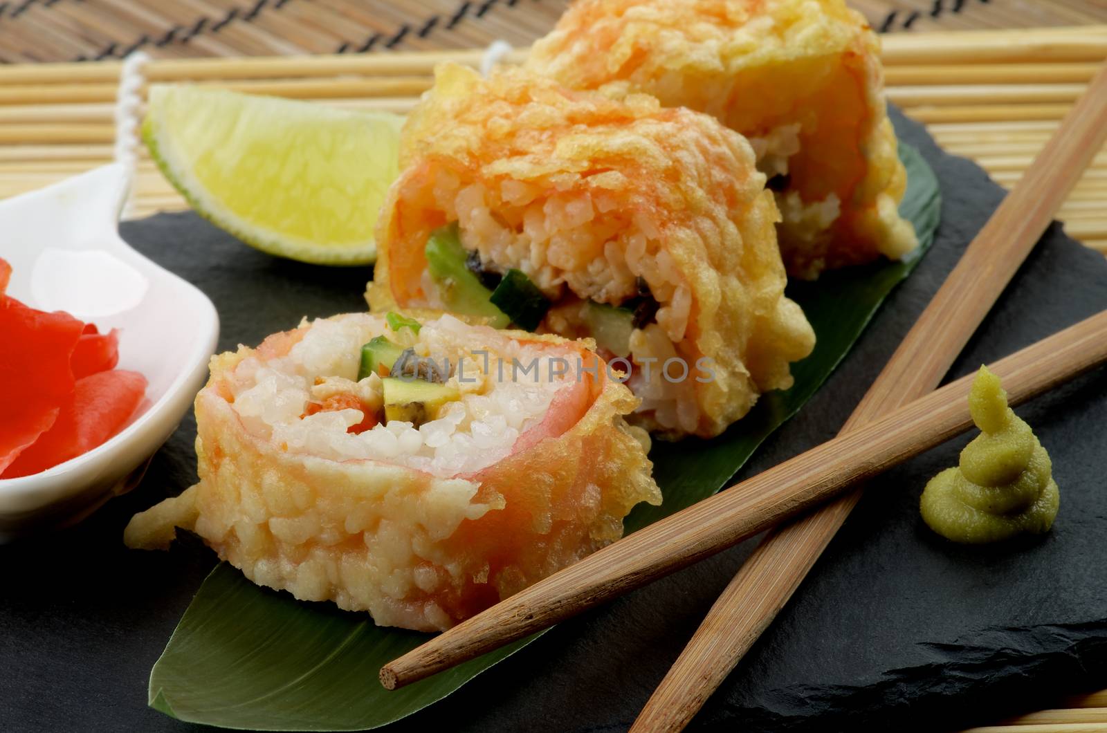 Hot Tempura Roll with Salmon and Avocado Served with Wasabi, Lime and Ginger on Black Plate with Chopsticks closeup. Focus on Foreground