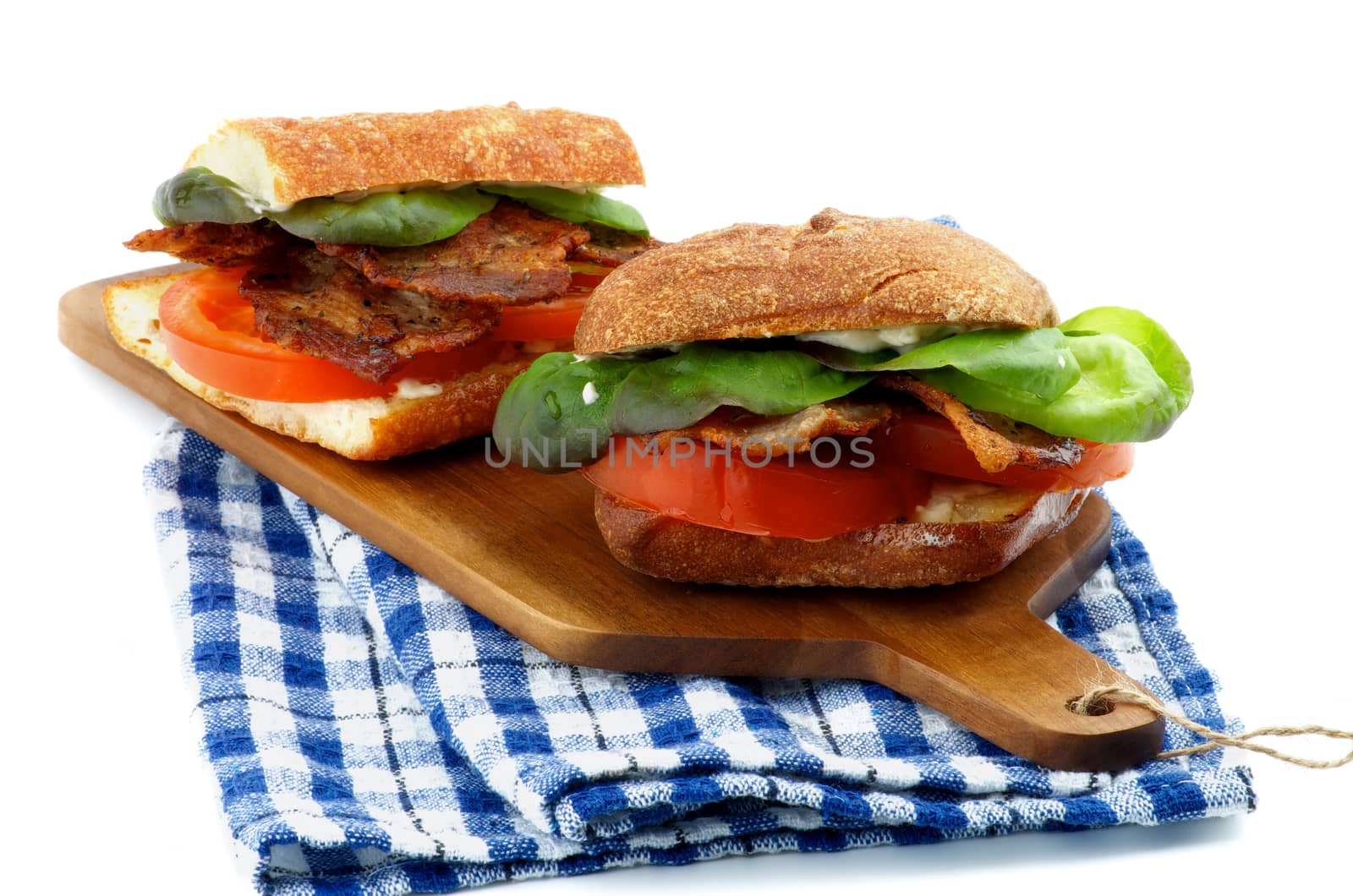 Tasty Ciabatta Sandwiches with Bacon, Tomato, Lettuce and Sauces on Cutting Board and Checkered Napkin isolated on white background