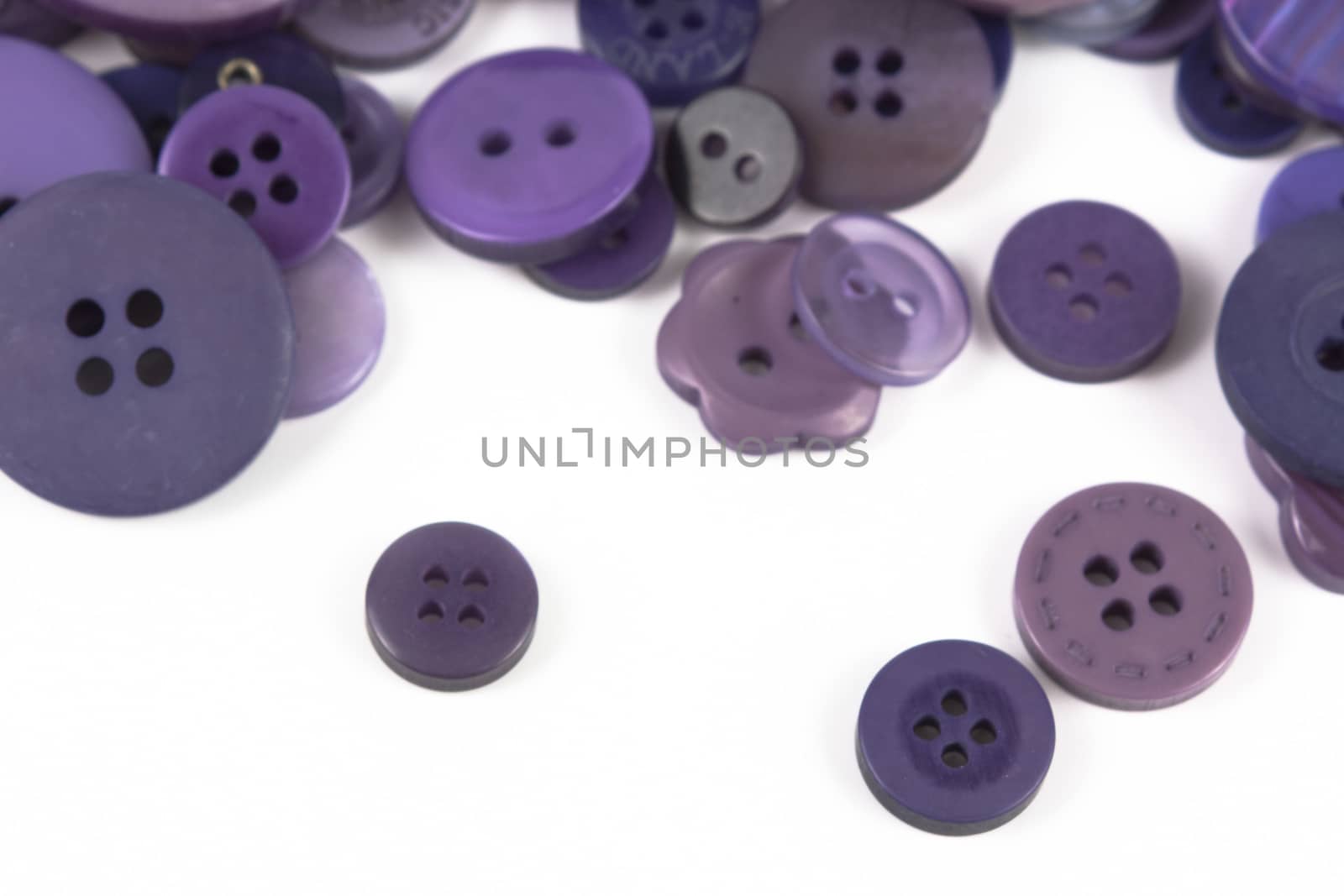 Close up of various purple button scattered on a white surface.