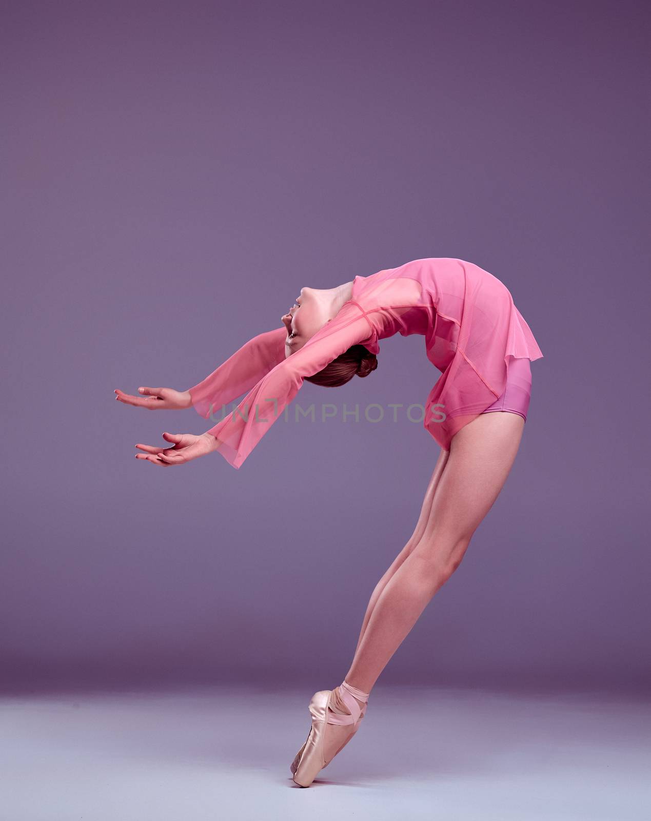 Young ballerina dancer in pink dress showing her techniques on lilac background