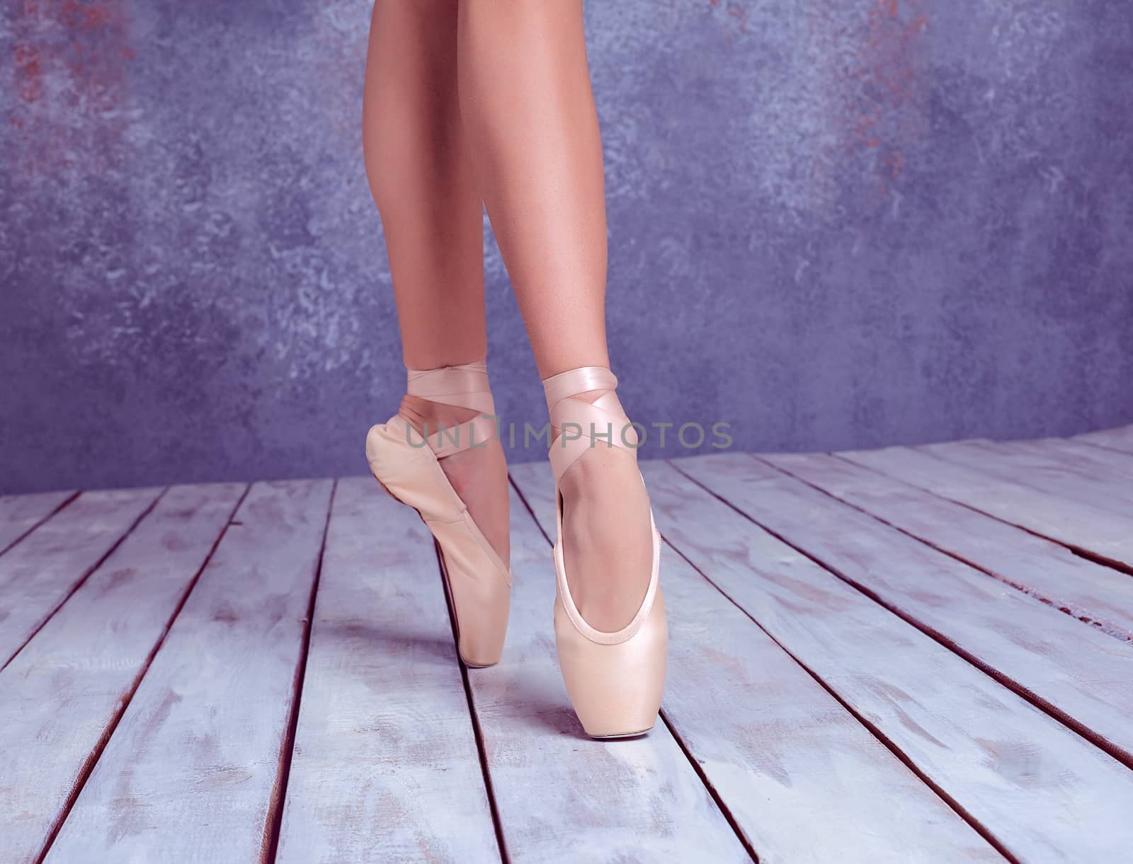The close-up feet of young ballerina in pointe shoes against the background of the wooden floor