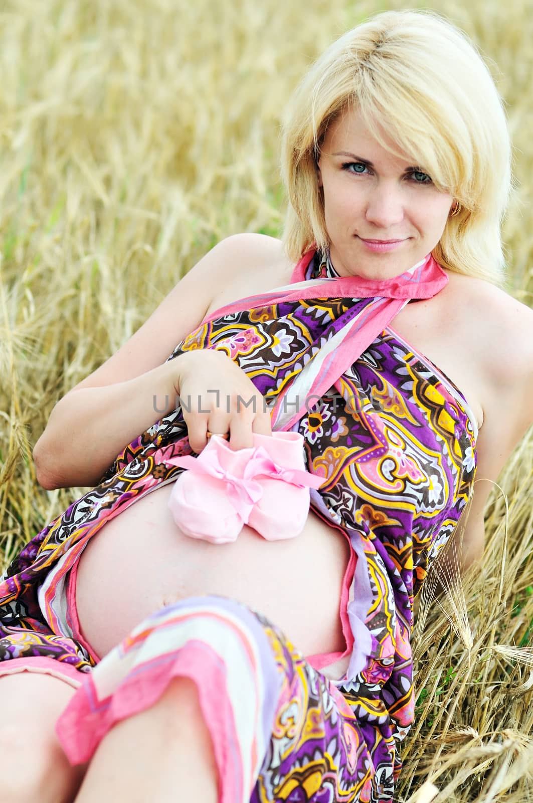 pregnant woman laying in wheat field and holding pink bootee 