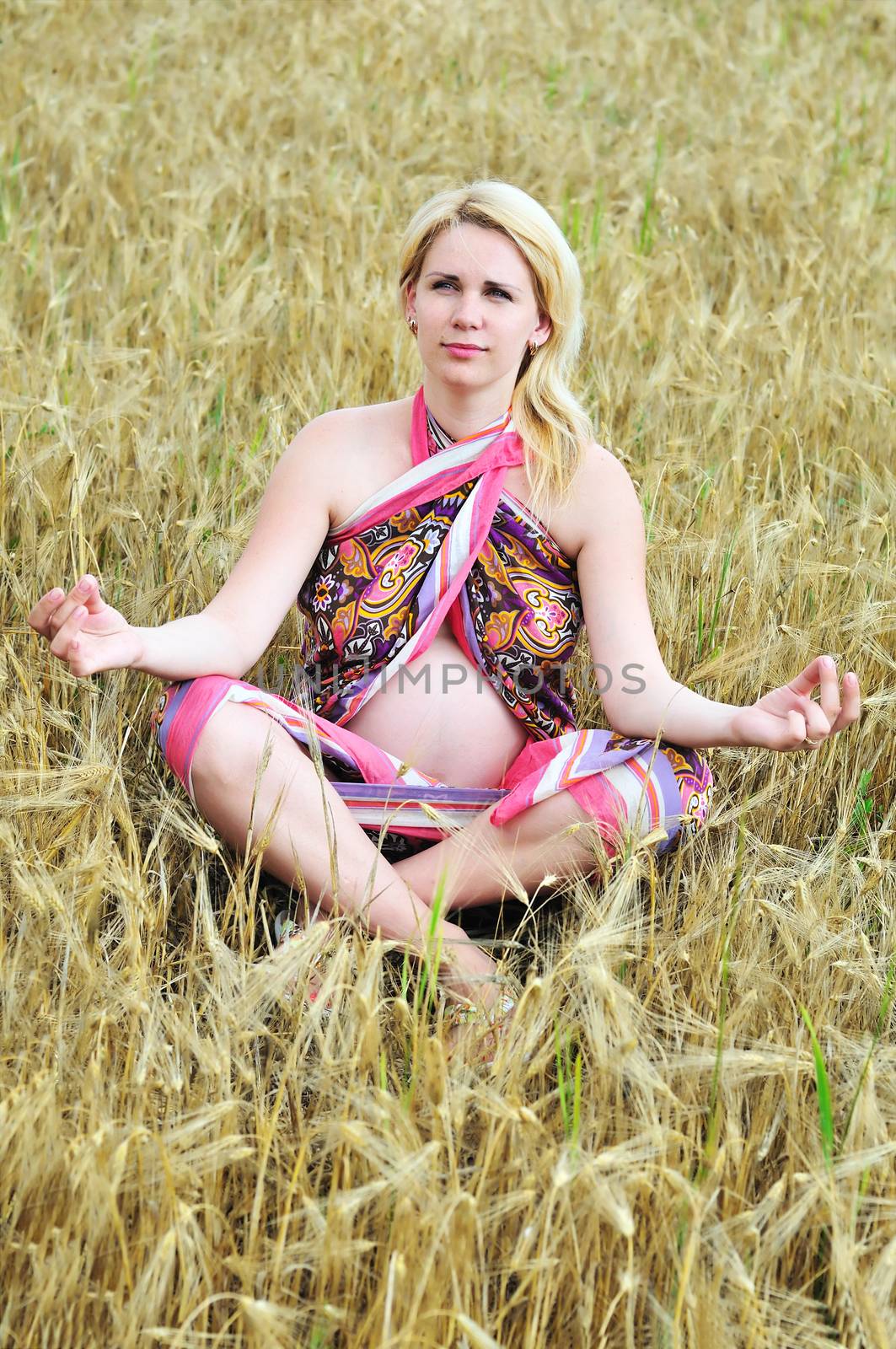 pregnant woman doing meditation in wheat field