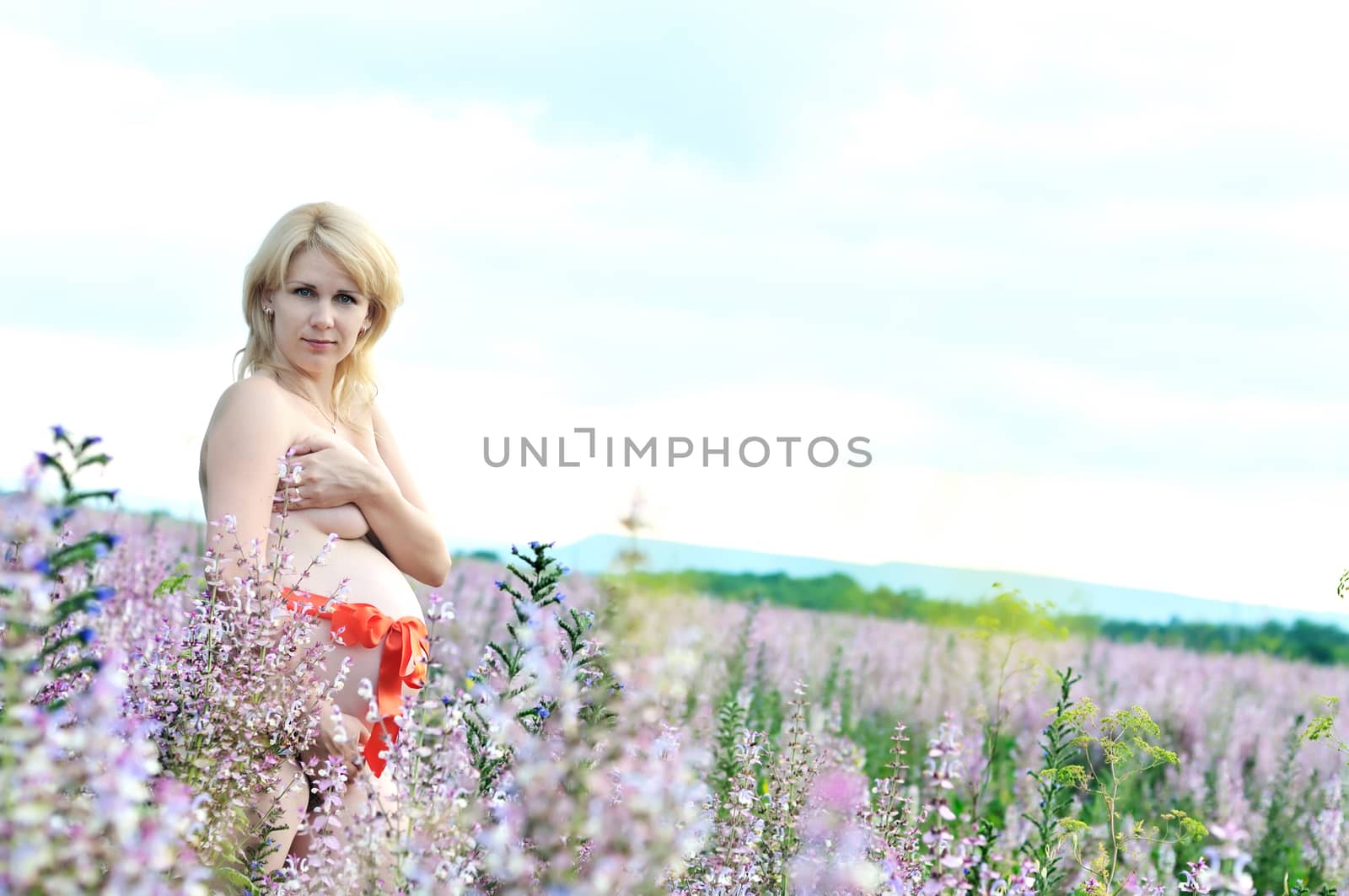 beauty blonde pregnant woman at one with nature with red belt on the belly