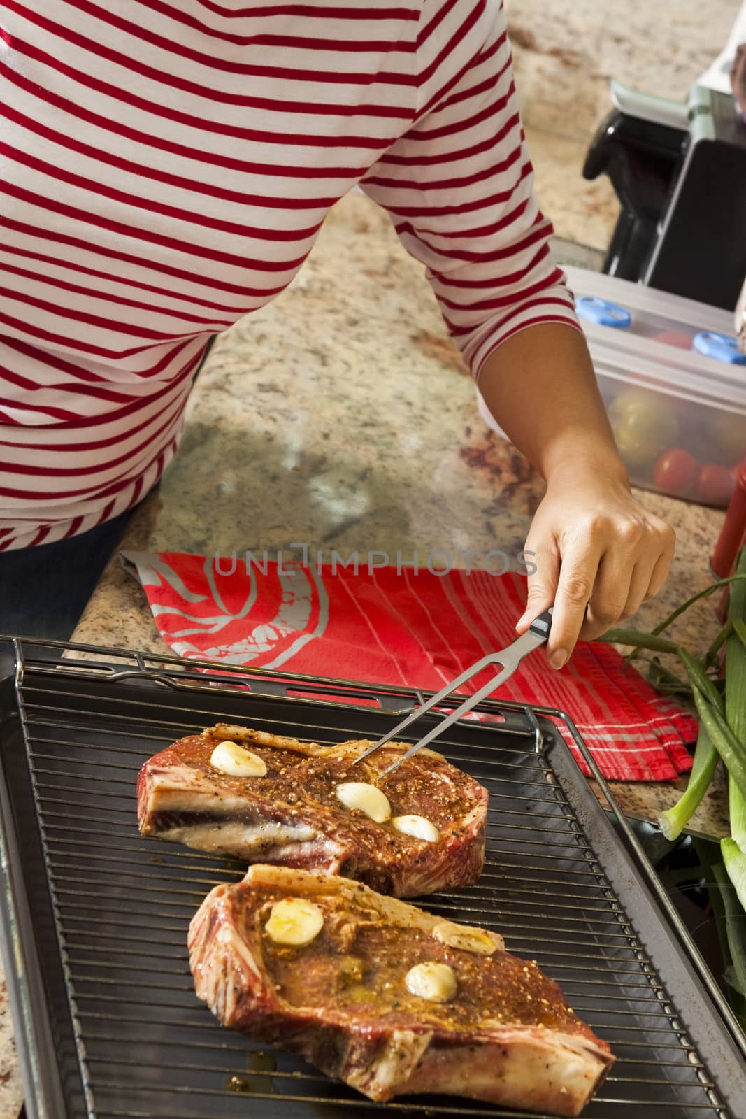 Attractive blond woman barbecuing meat outdoors in the garden grilling two marinated spicy beef steaks over a fire