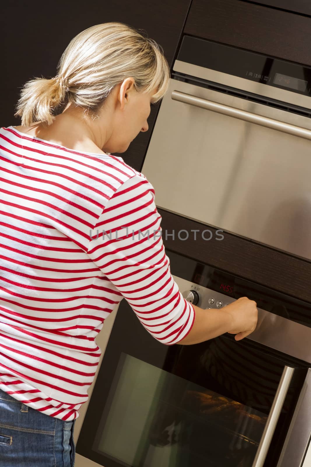 Attractive blond woman barbecuing meat outdoors in the garden grilling two marinated spicy beef steaks over a fire