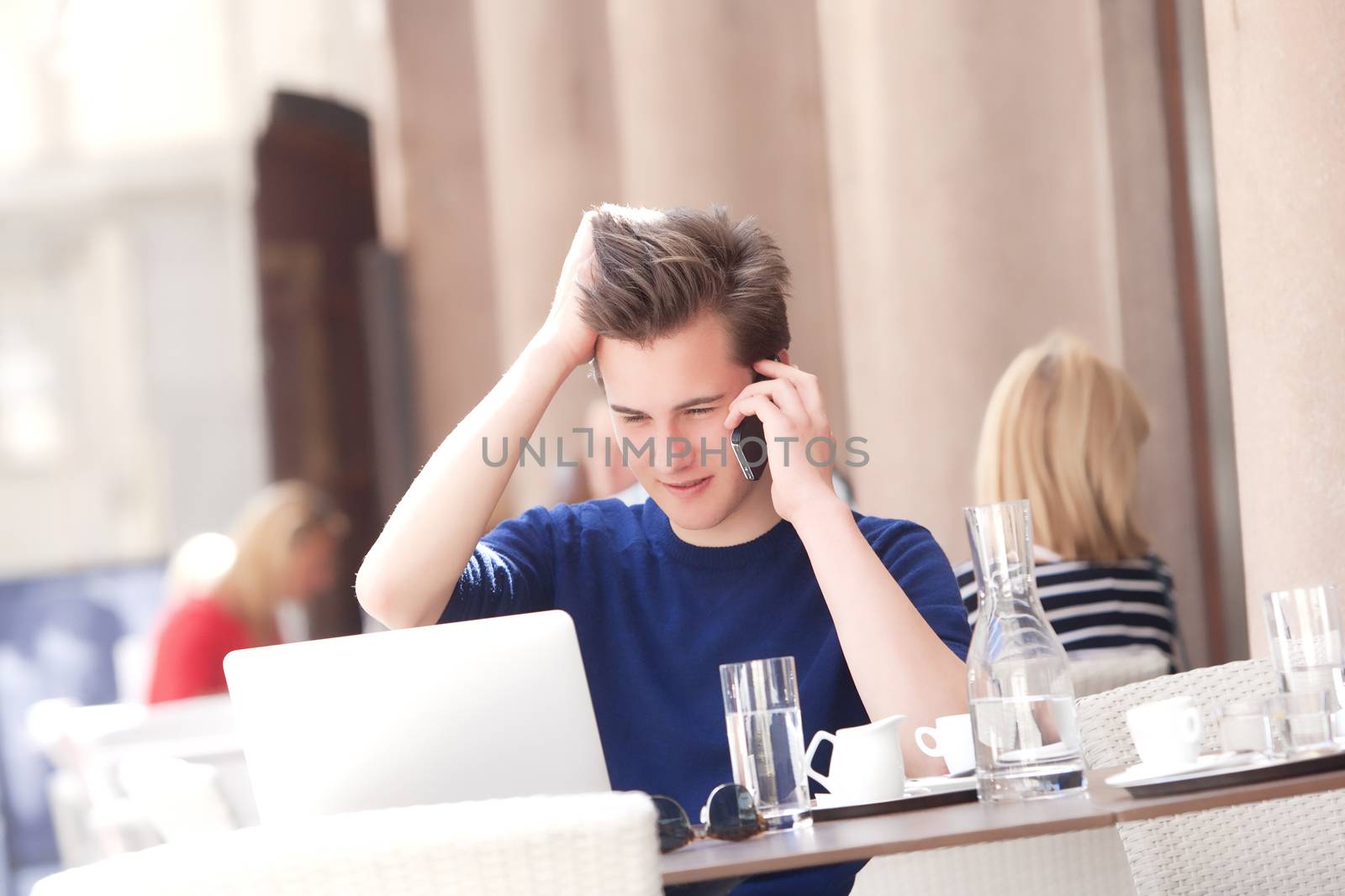 Young Man Sitting in Outside Coffeehouse Talking on Phone by courtyardpix