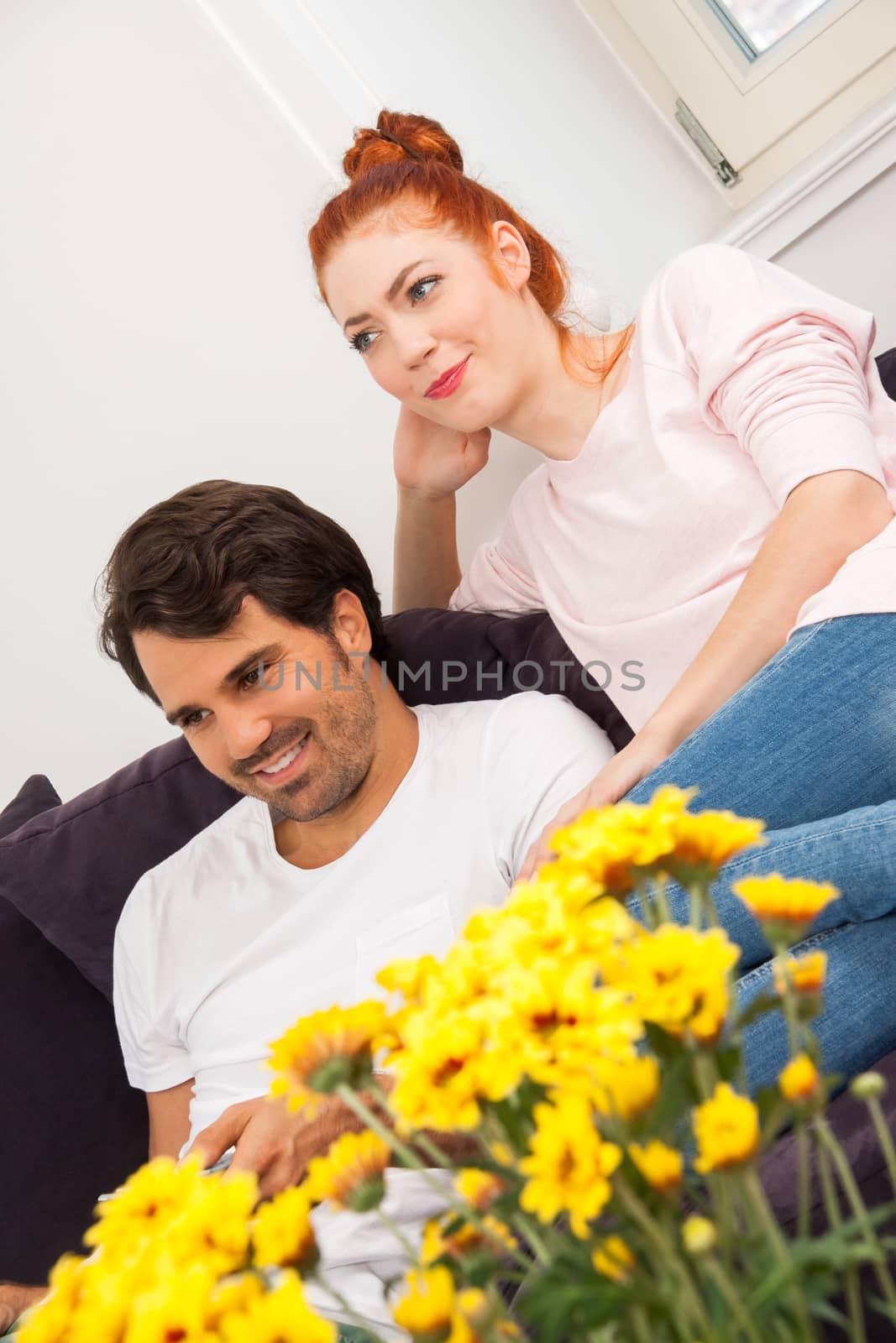 Close up Happy Young Couple Sitting on the Couch at the Living Room While Looking Something Into Distance.