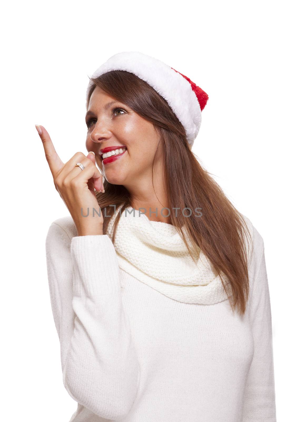 Attractive smiling woman in a festive red Santa hat pointing towards blank copyspace for our Christmas advertising, text or seasonal greeting, isolated on white
