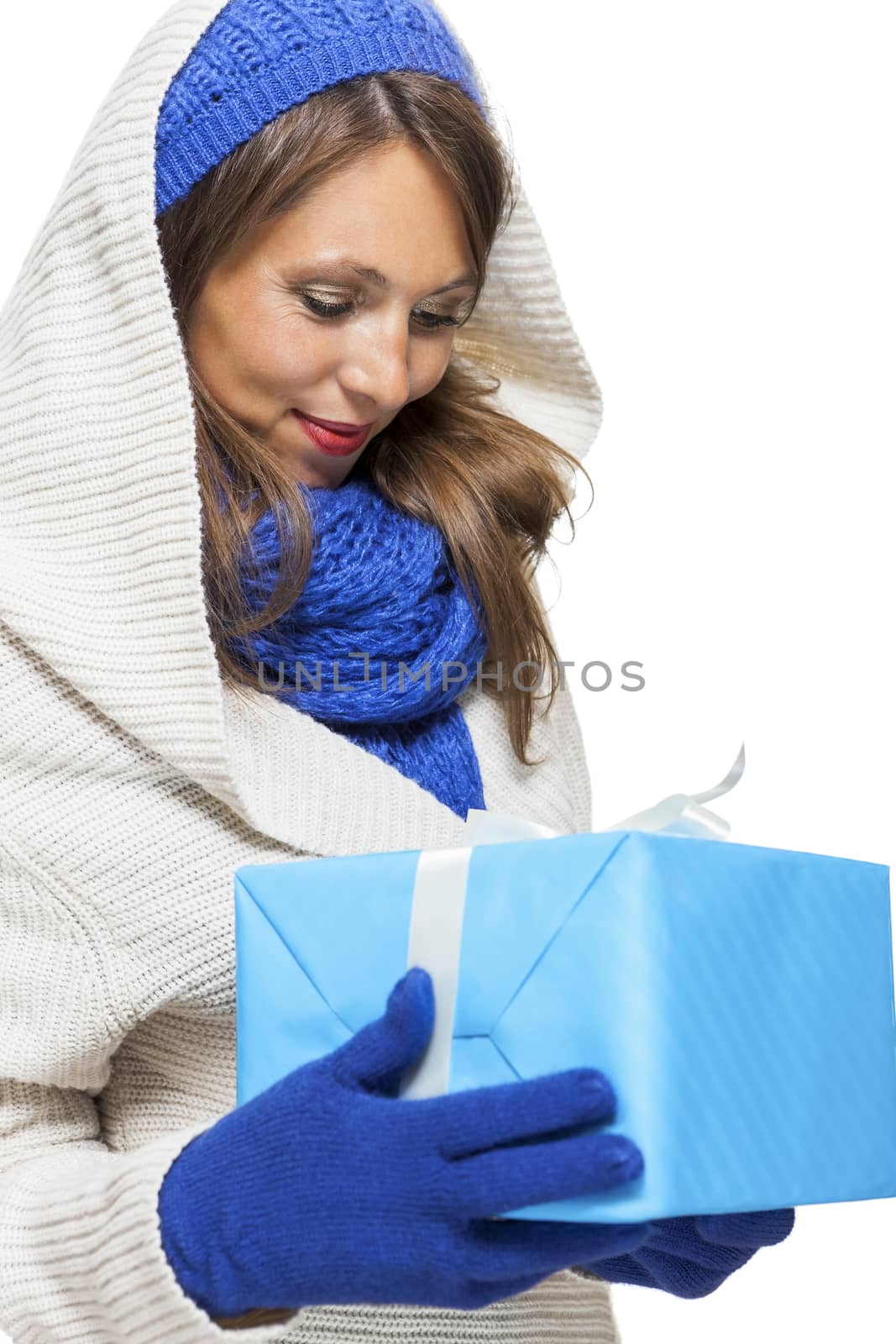 Young woman in fashionable blue knitted winter fashion accessories holding a matching blue gift in her hands looking down at it with a pleased smile, isolated on white