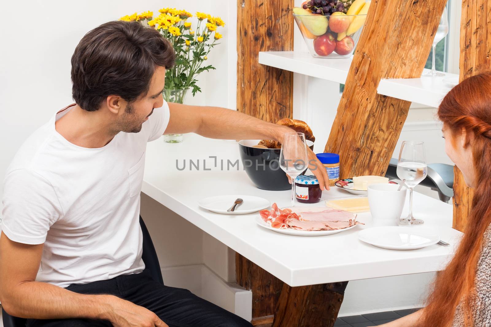 Young Couple Sitting at the Table and Slicing Freshly Baked Bread for their Ham Sandwich.