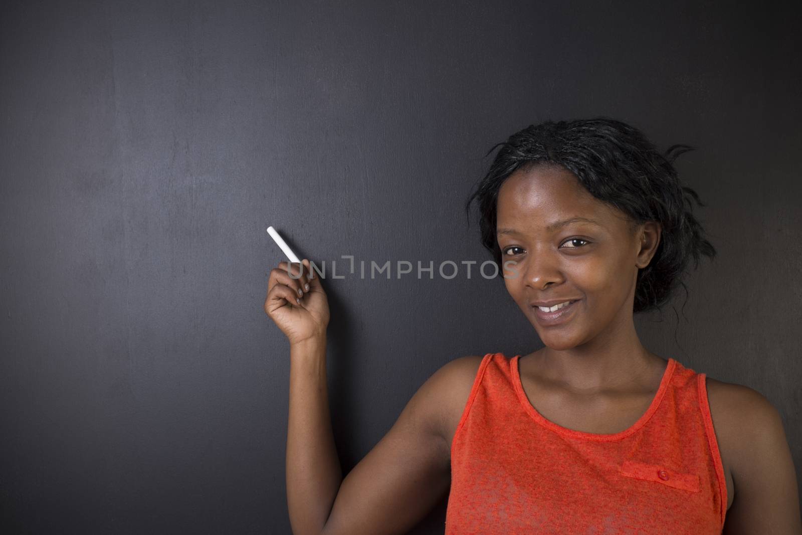 South African or African American woman teacher or student holding or pointing chalk on blackboard background