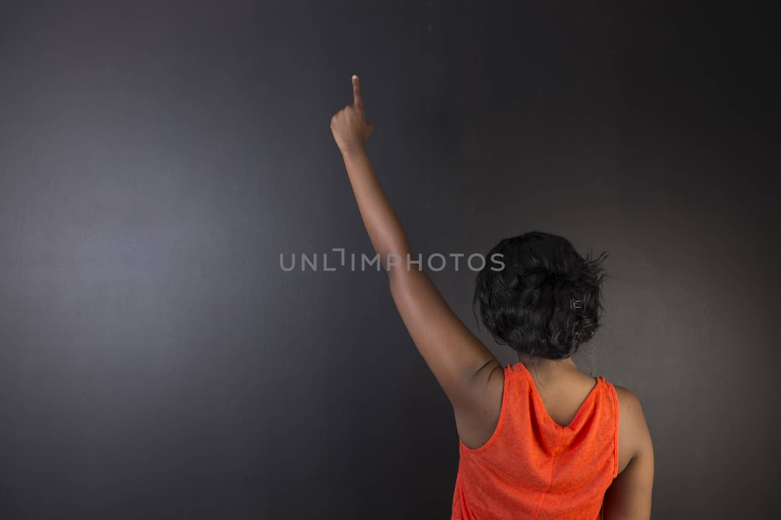 South African or African American woman teacher hand up on chalk black board background by alistaircotton