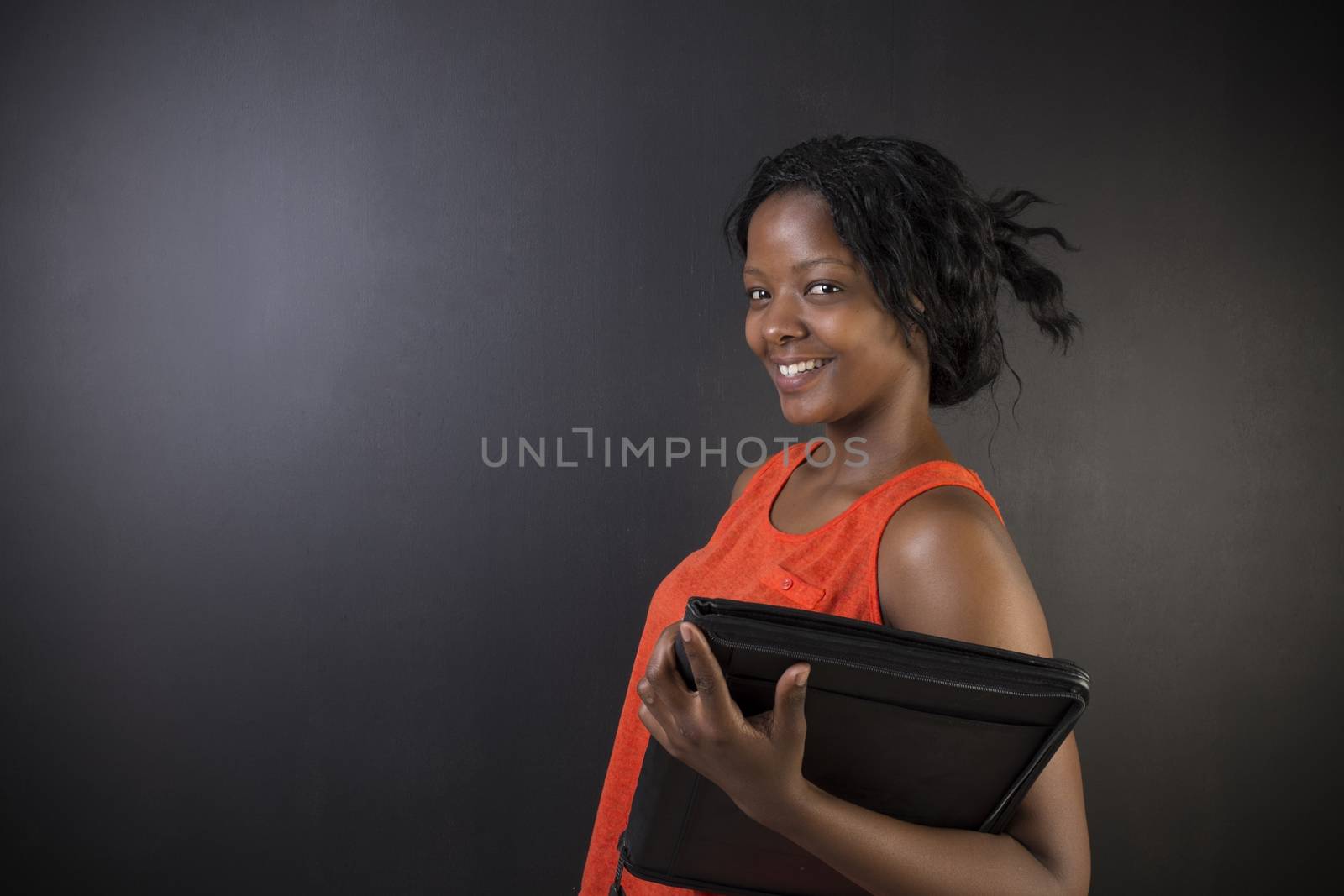 South African or African American woman teacher or student with notepad against a blackboard background