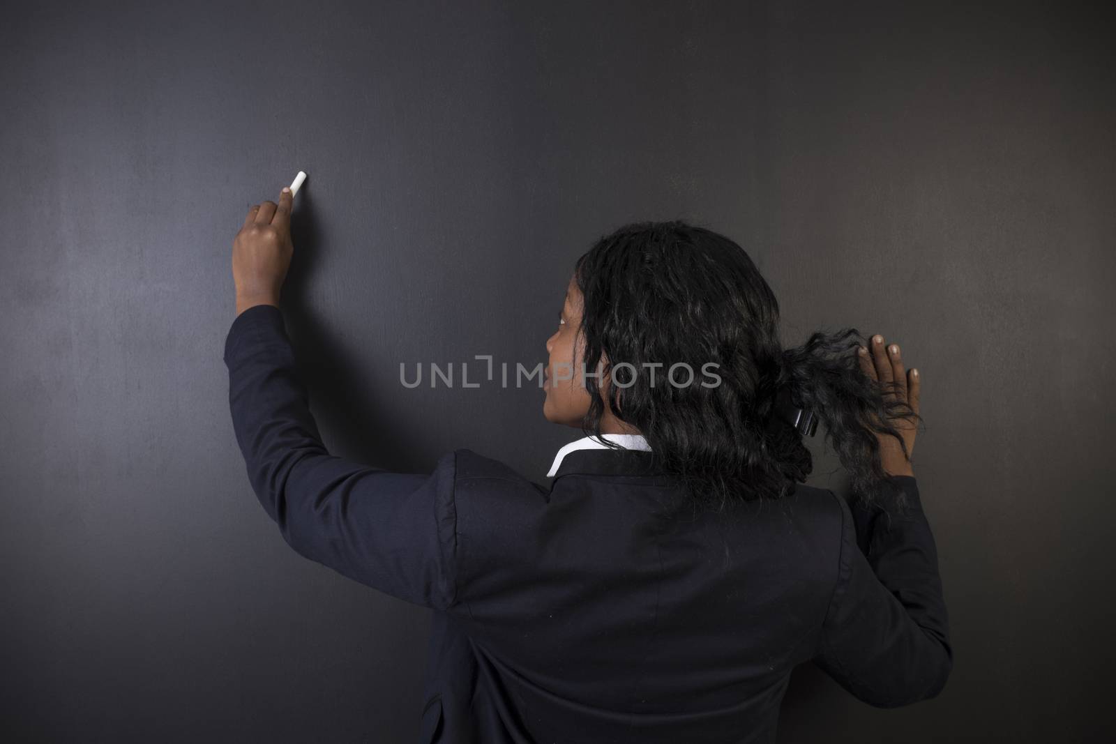 South African or African American woman teacher writing on chalk black board background by alistaircotton