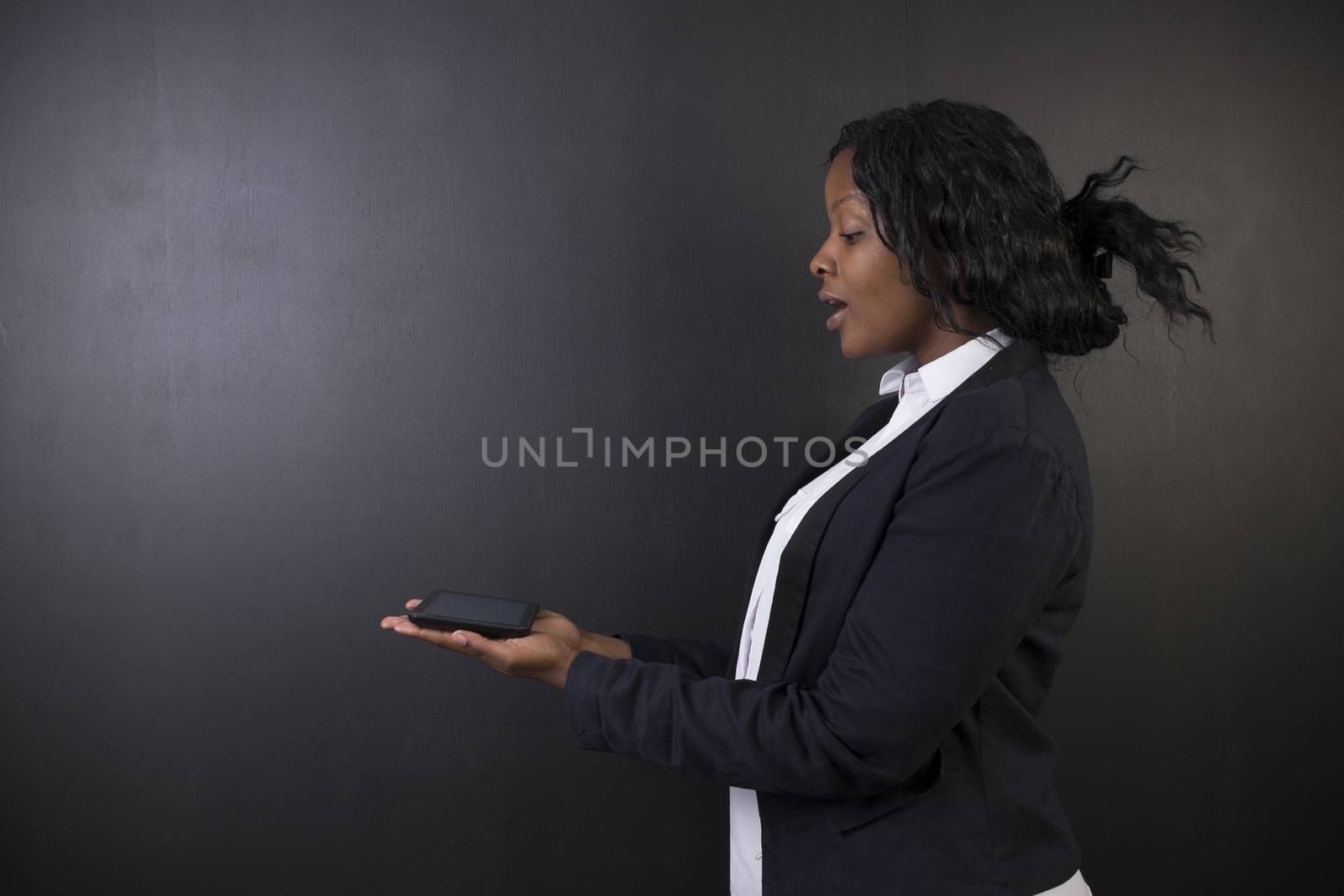 South African or African American woman teacher or student holding computer tablet on blackboard background