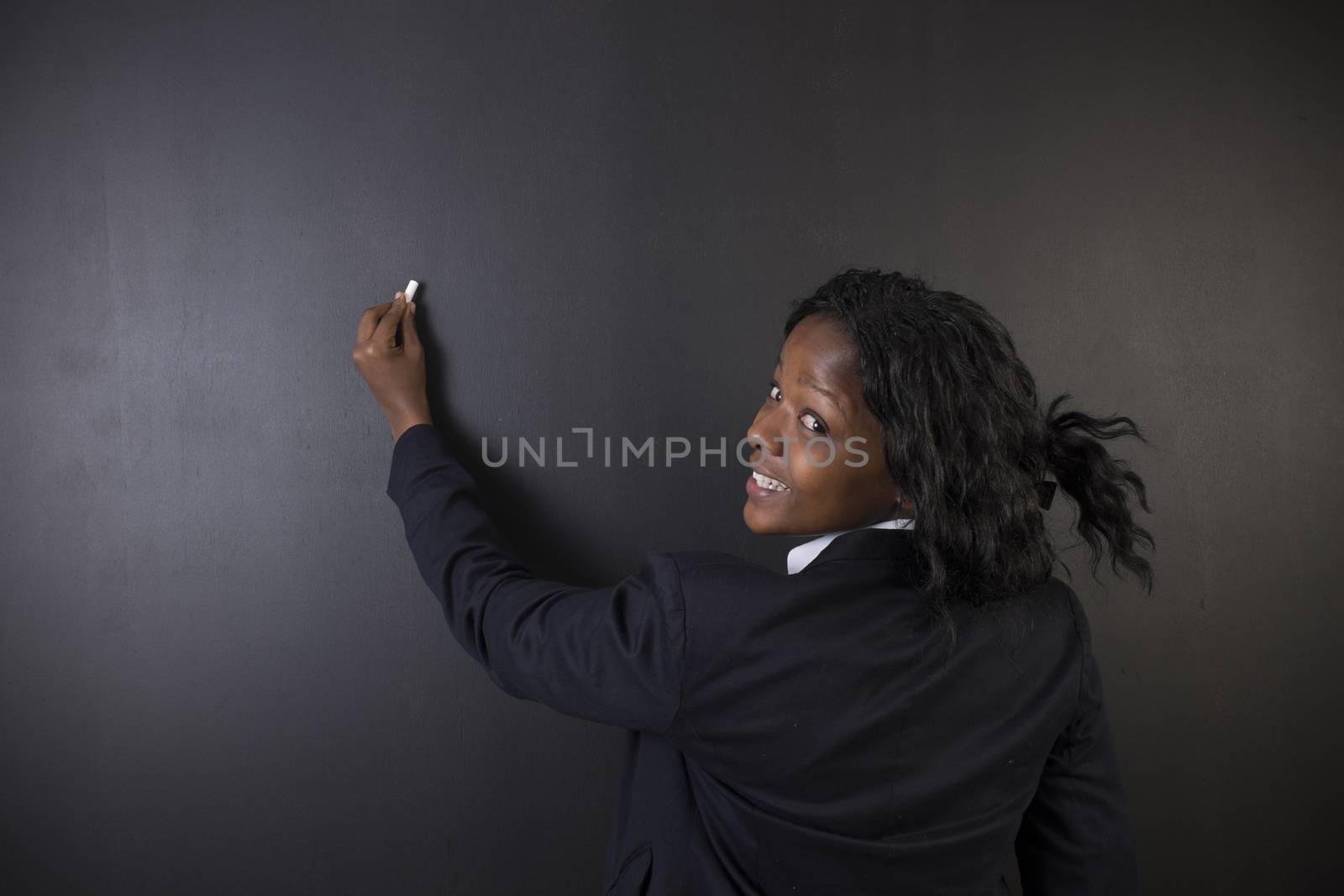 South African or African American woman teacher or student writing on chalk black board background