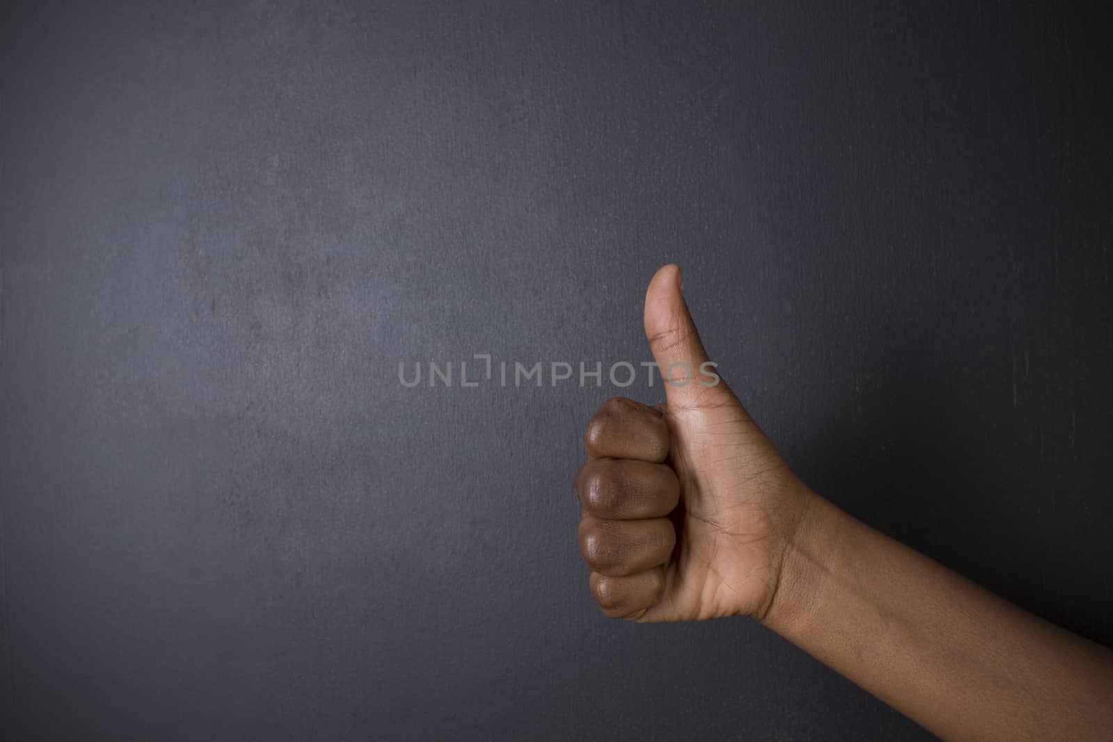 South African or African American woman teacher or student with thumb up on chalk black board background