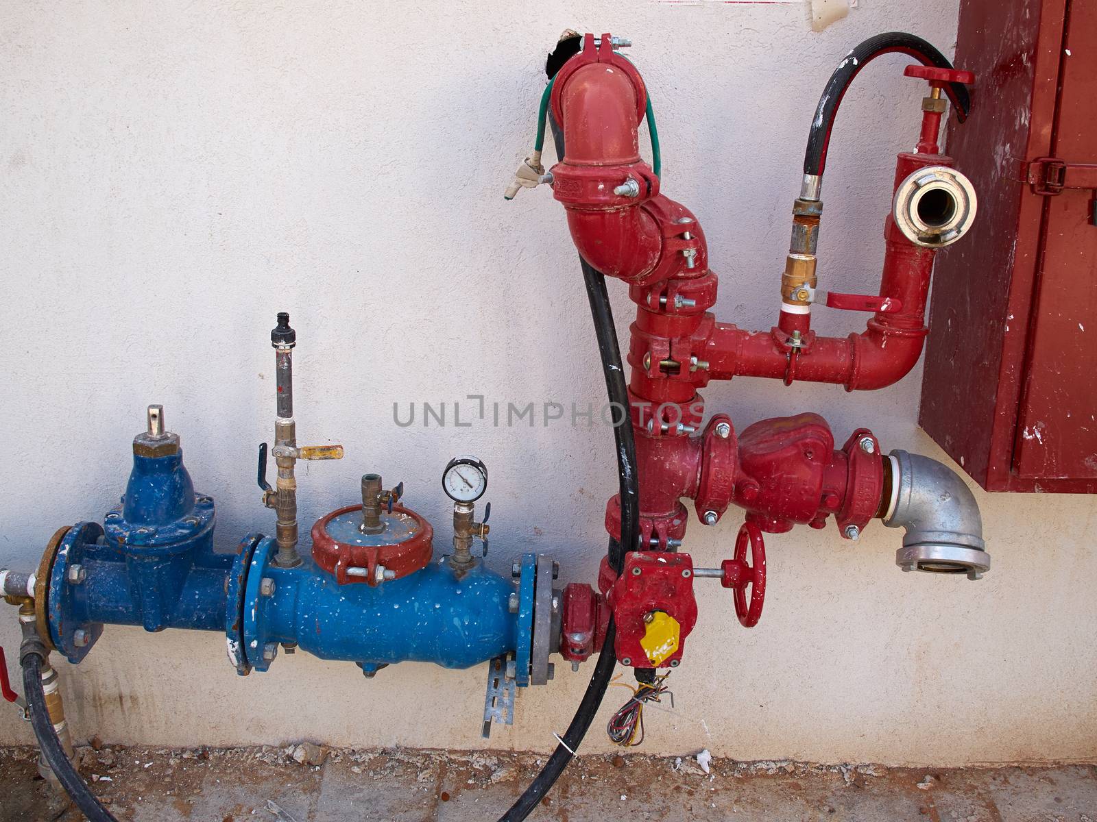 Blue and red metal industrial water pipes with a valve against a wall