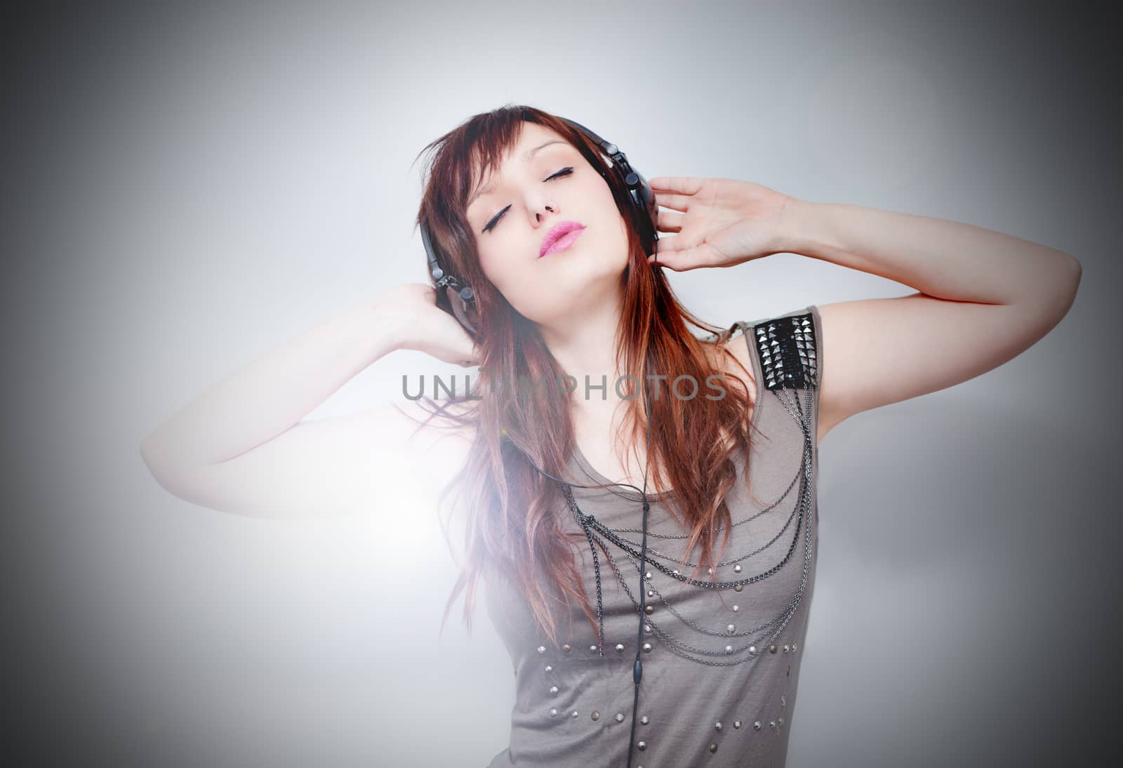 Beautiful young woman listening to music with headphones on background with stage lights. Music live