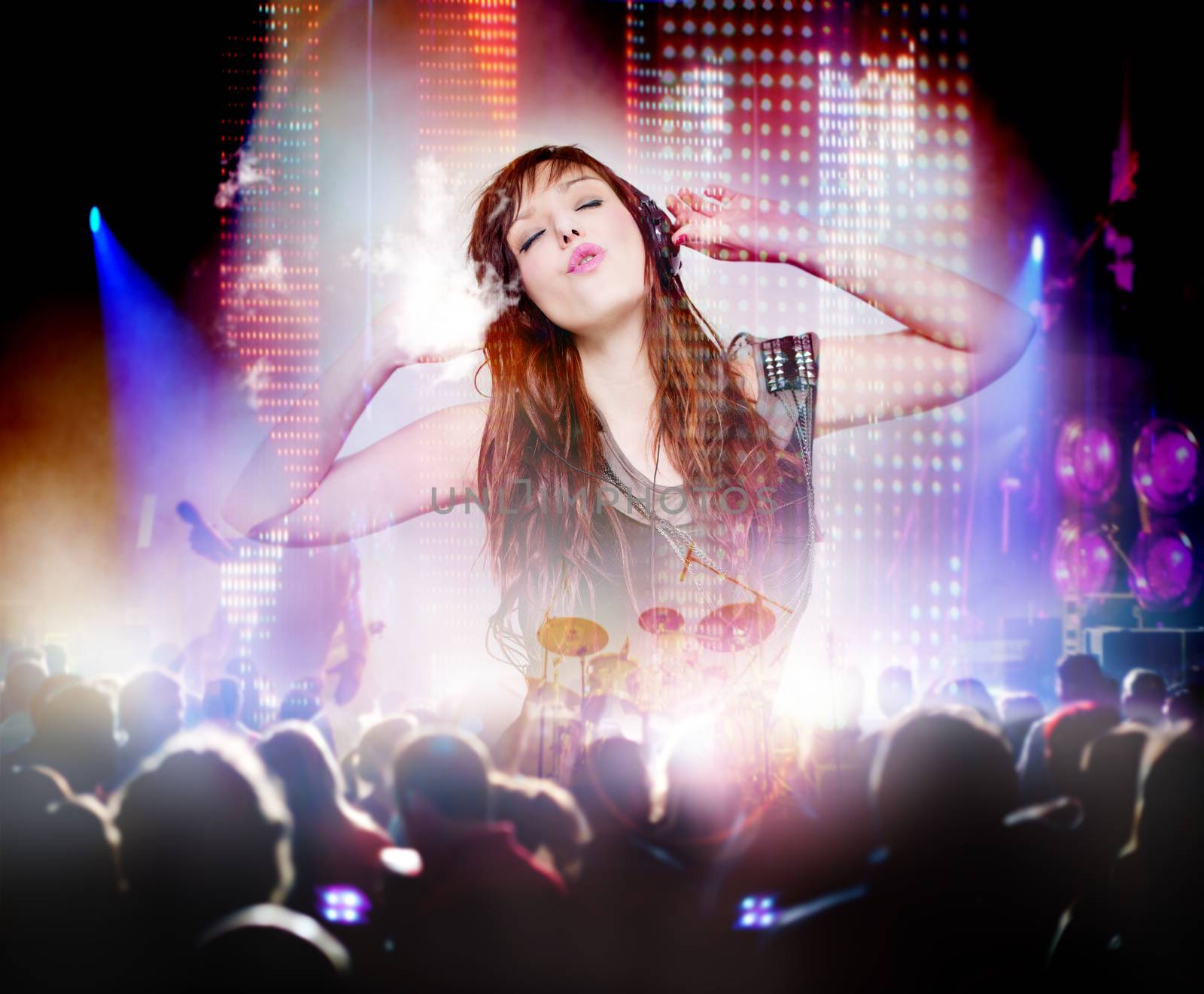 Beautiful woman listening to music with headphones and silhouettes of concert crowd in front of bright stage lights. Concept background of live music and party