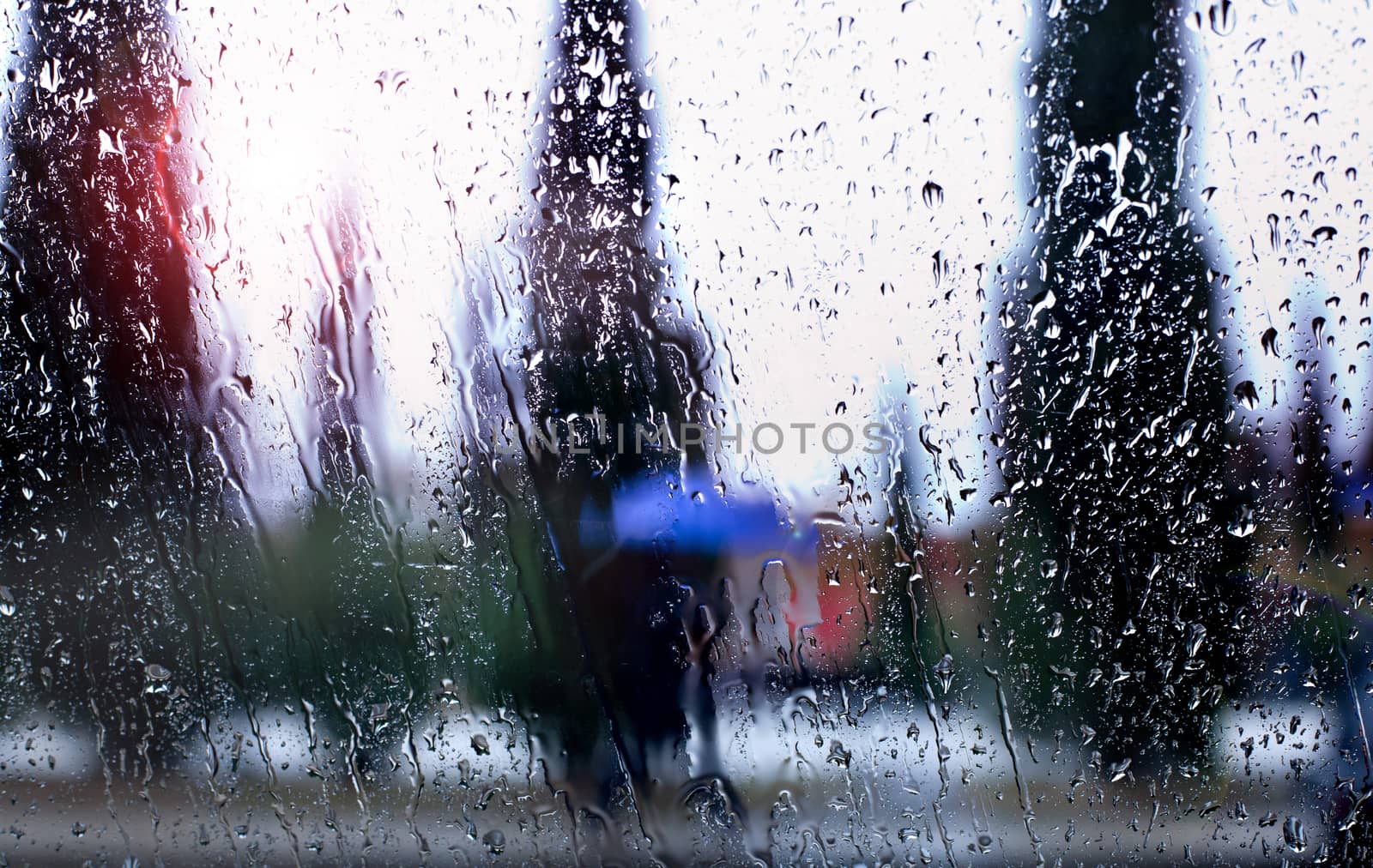 abstract image of falling rain drops through the window with city background by Ainat