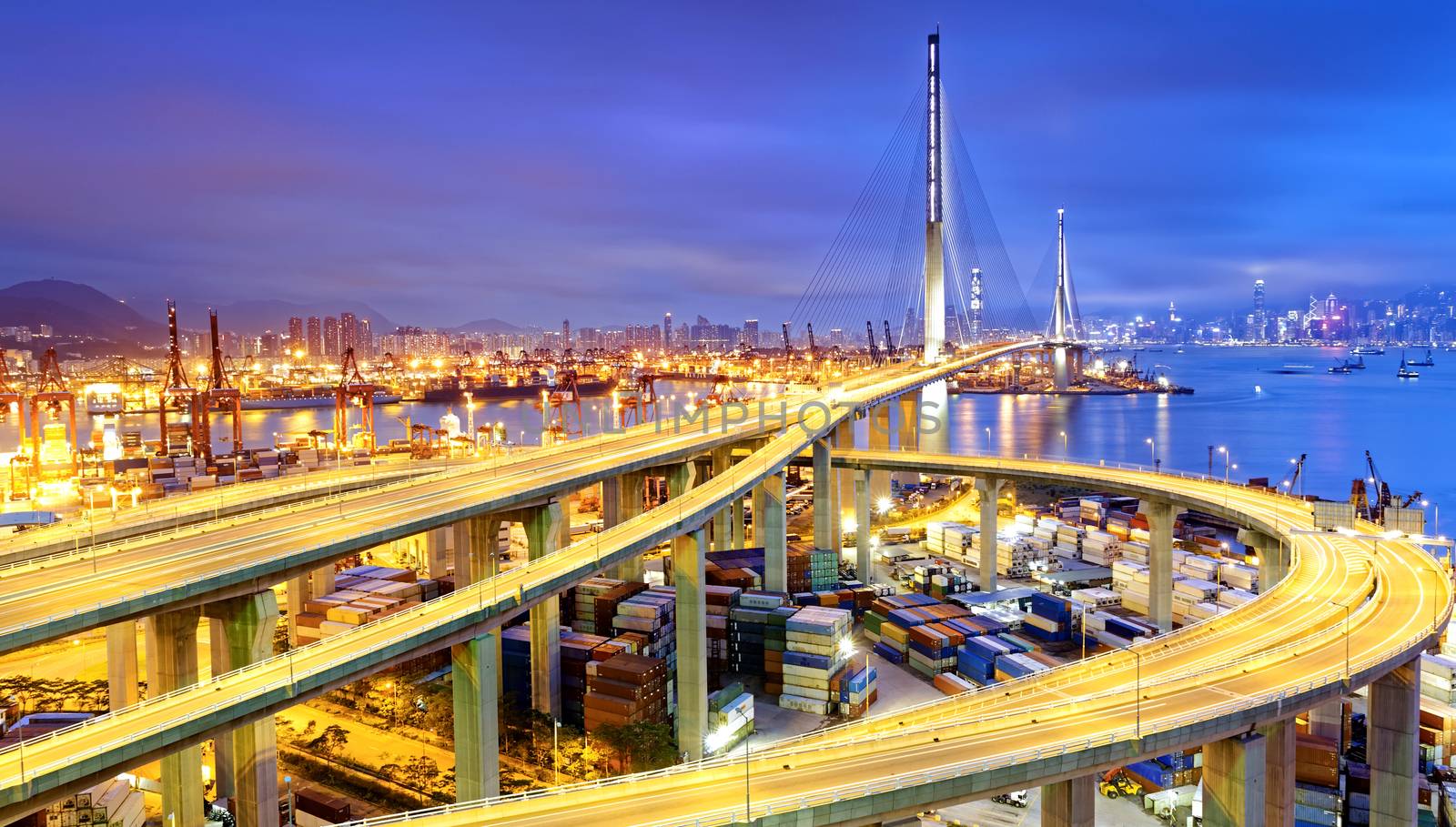 Container Cargo freight ship with working crane bridge in shipyard under Stonecutters highway bridge at sunset for Logistic Import Export, Hong kong