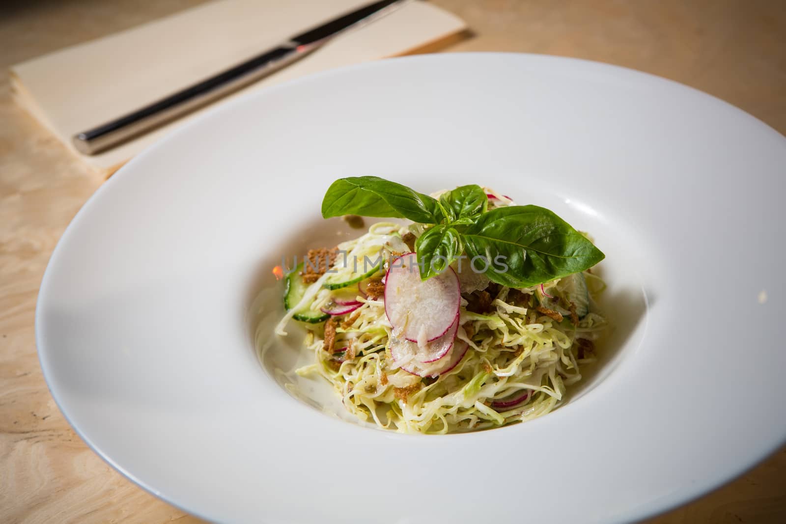 Salad from cabbage, herbs, cucumber, onion and radish in bowl on green wooden background. Coleslaw. Selective focus.