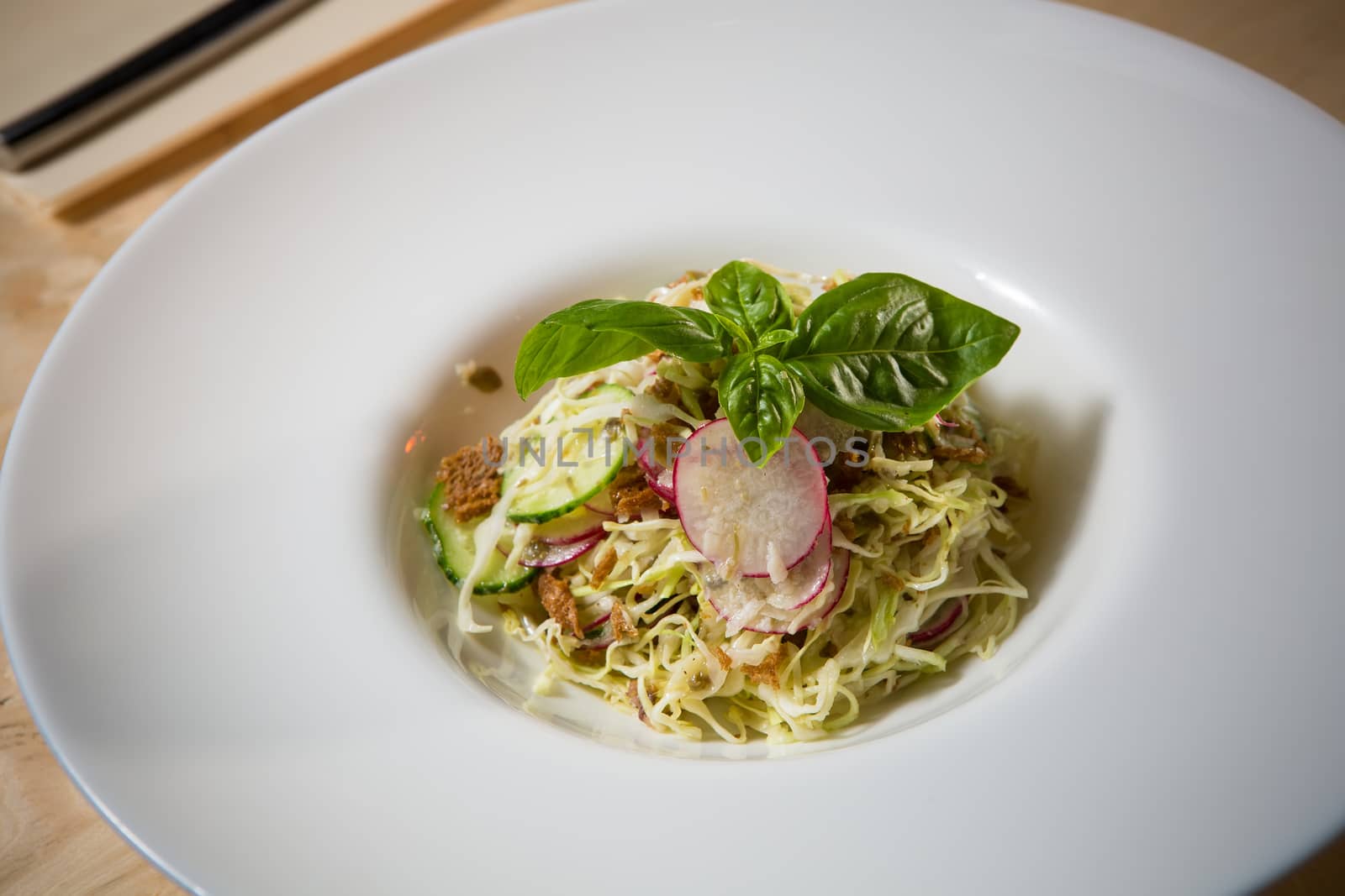 Salad from cabbage, herbs, cucumber, onion and radish in bowl on green wooden background. Coleslaw. Selective focus.